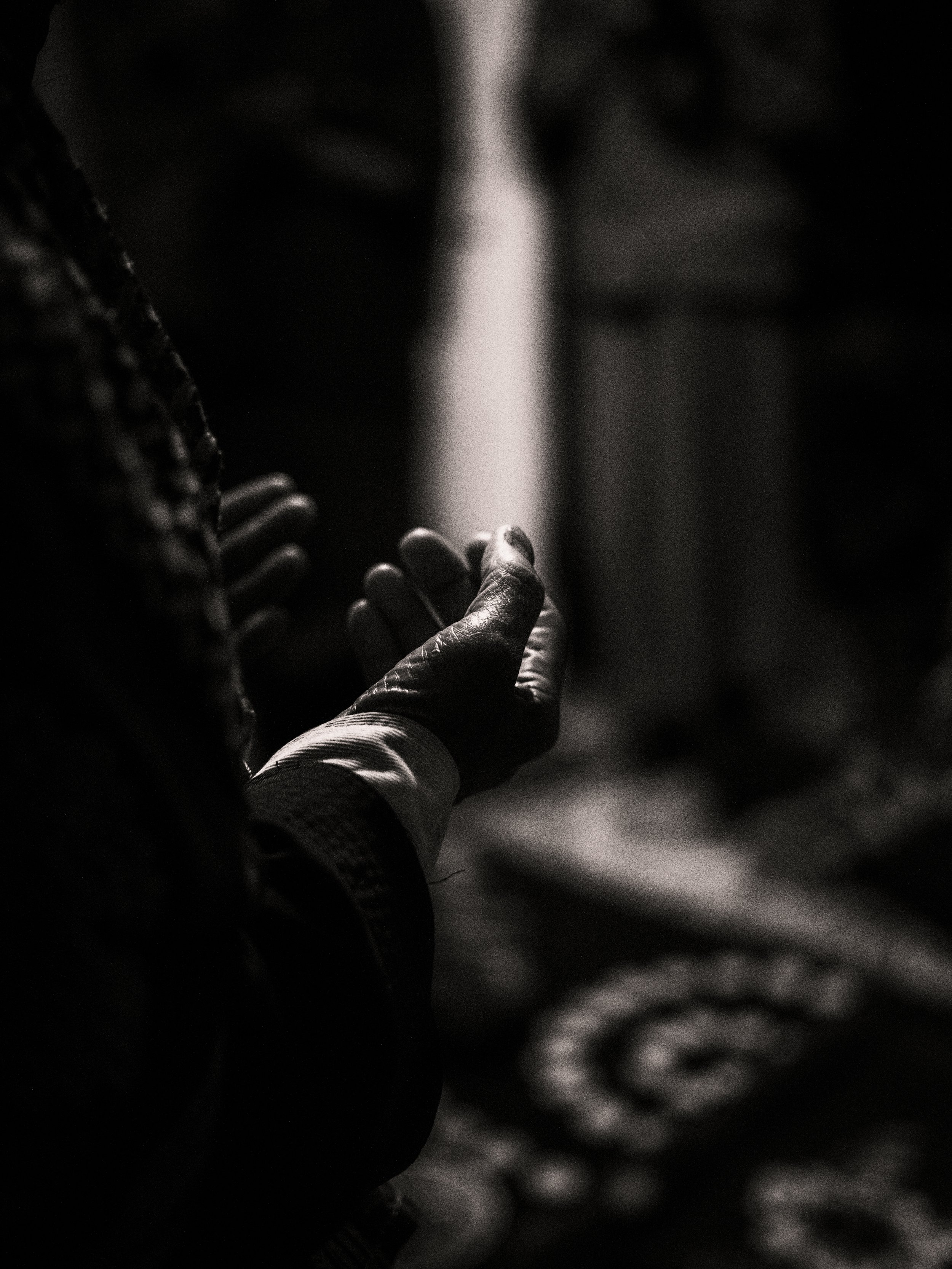 A close-up black and white photo of a person's hand with fingers pressed together, resting on their chest, next to their face in a reflective posture.