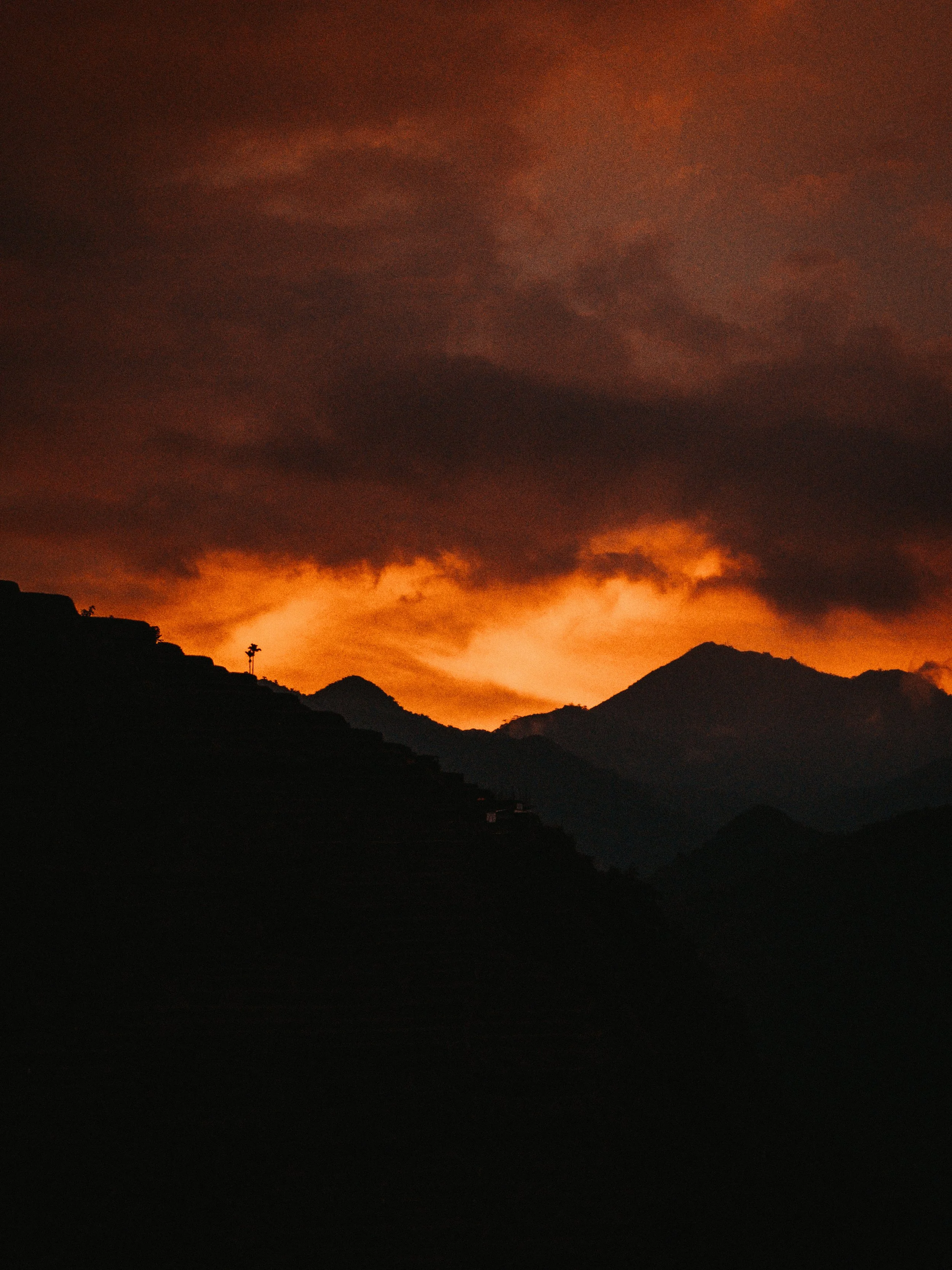 A silhouette of mountains at sunset with an orange and red sky and dark clouds.