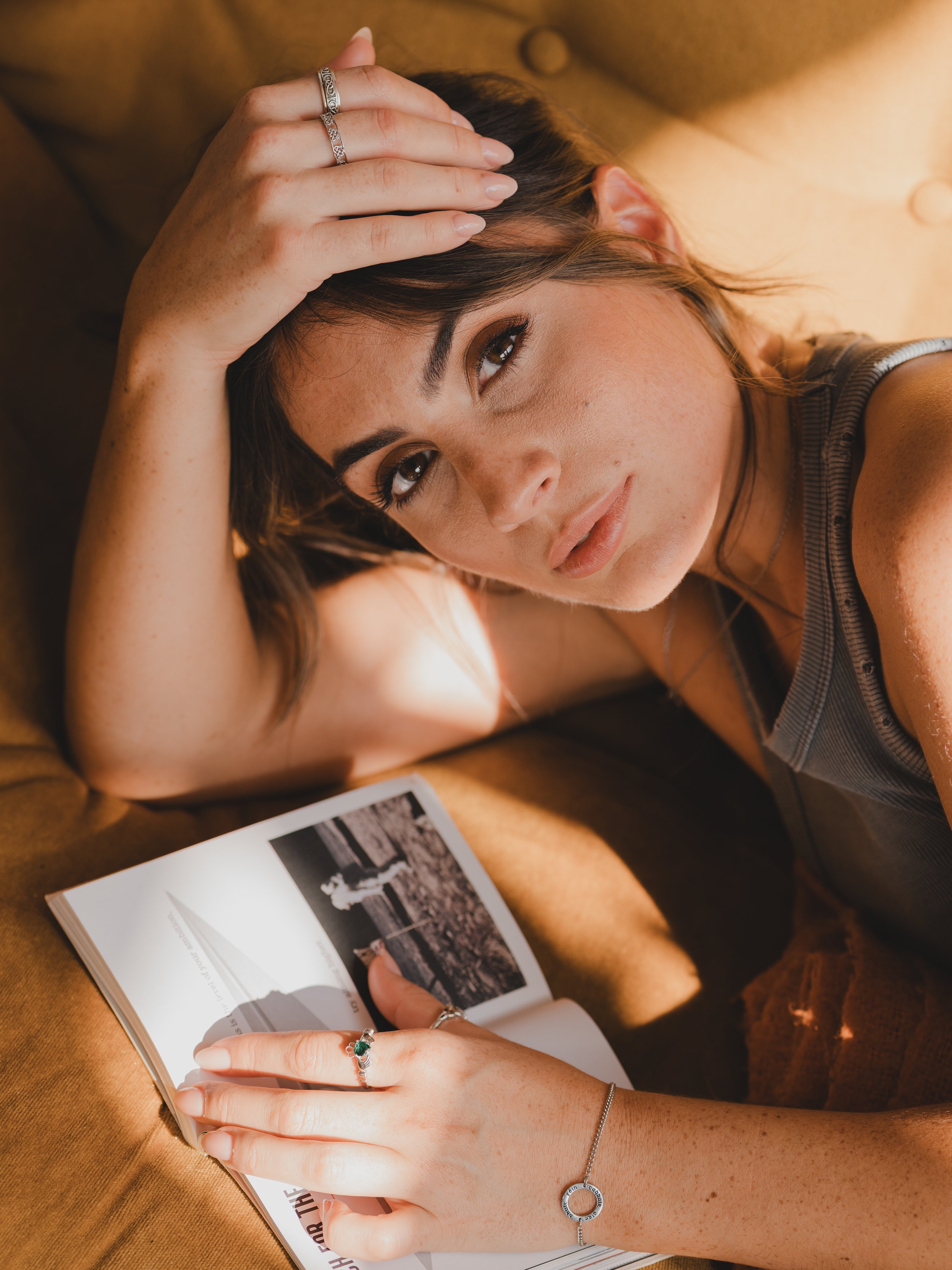 A young woman with brown hair and freckles lying on a tan couch, resting her head on her hand and looking at the camera, with an open photo album nearby.