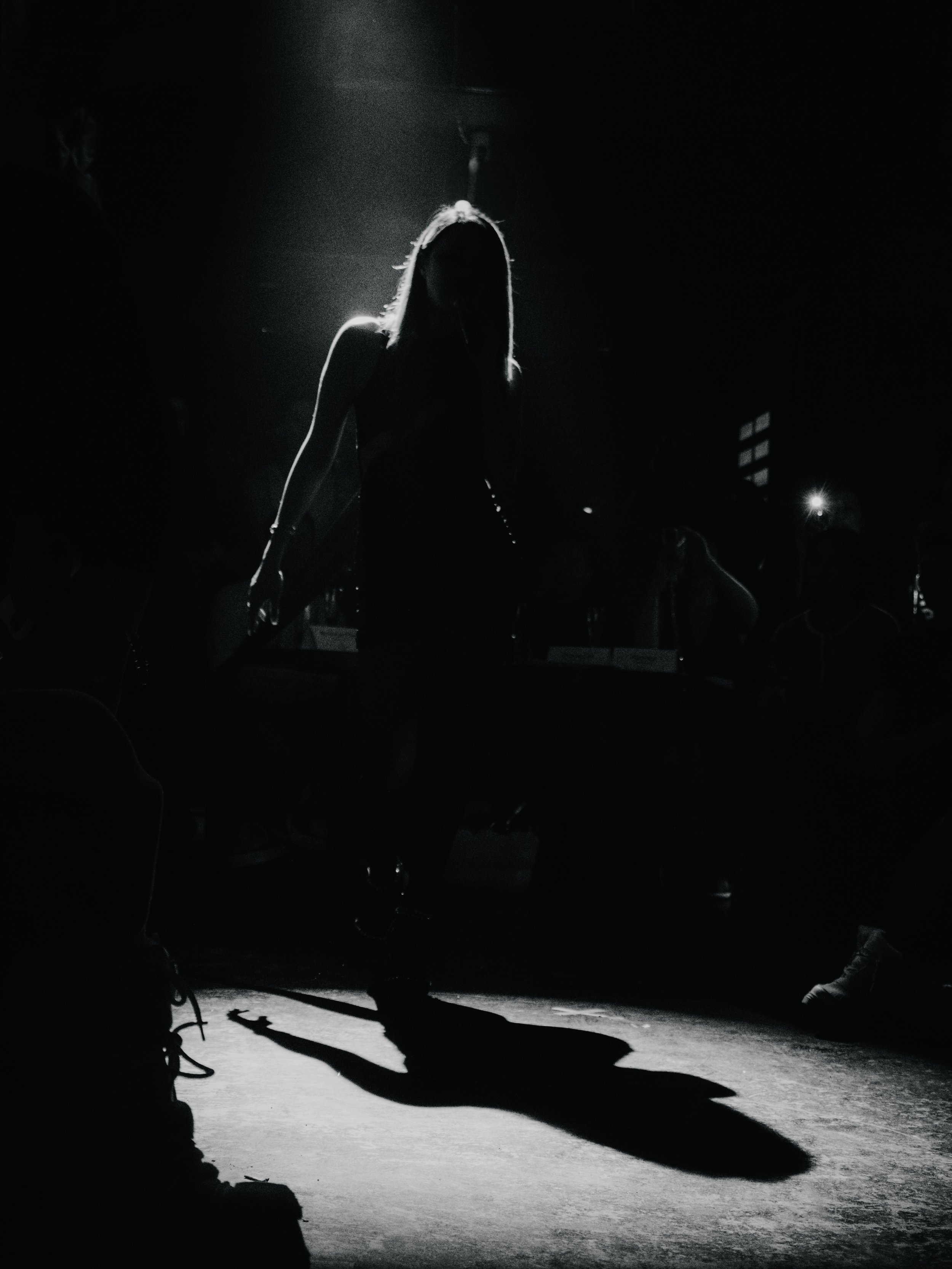 A silhouette of a woman standing with sunlight behind her, creating a shadow on the floor in a dark room.
