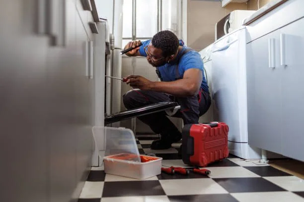 A man repairing a washing machine in a laundry room, kneeling on the floor with tools and a red toolbox nearby.