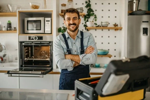 A man with a beard smiling in a modern kitchen with appliances and shelves in the background.