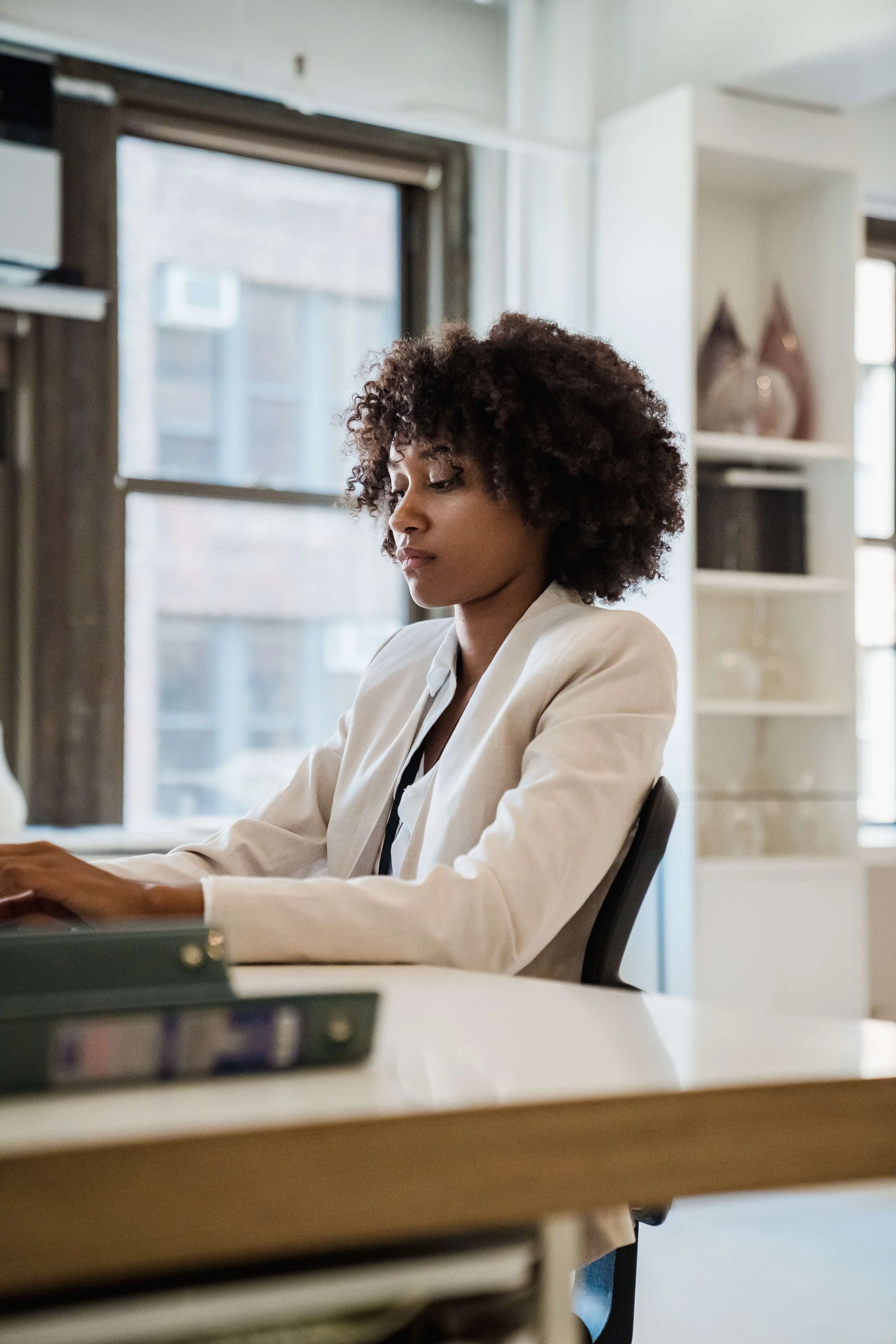 A woman with curly hair working at her desk in a bright, modern office.