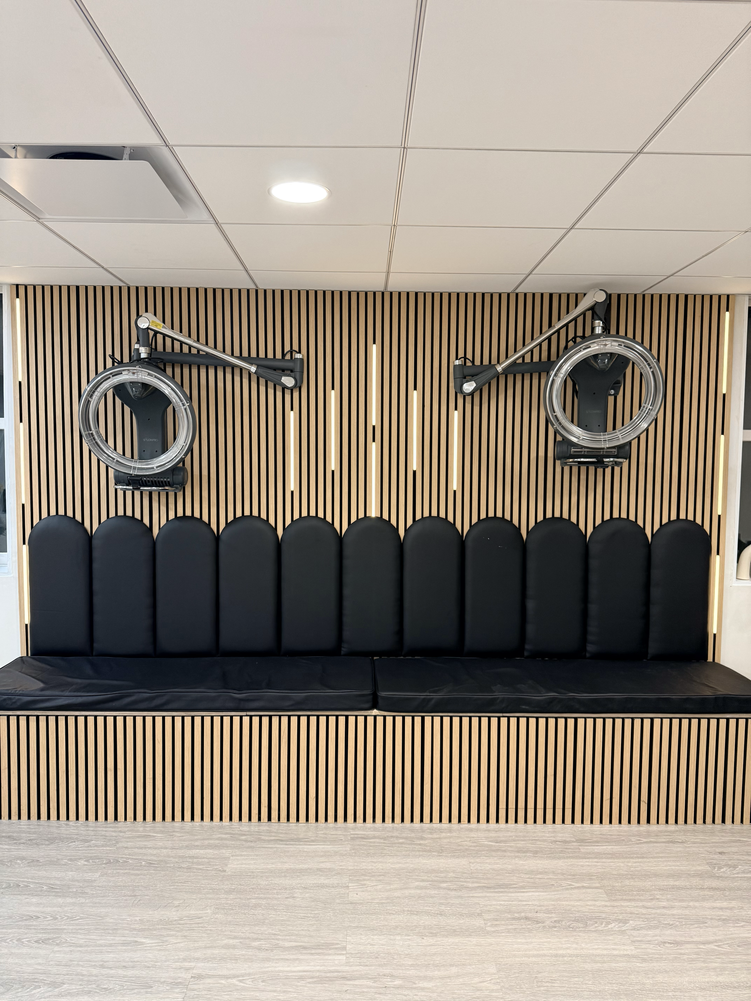 Room with black cushioned bench and modern wall-mounted medical equipment, including two large circular devices with arms, against a wooden slat wall.