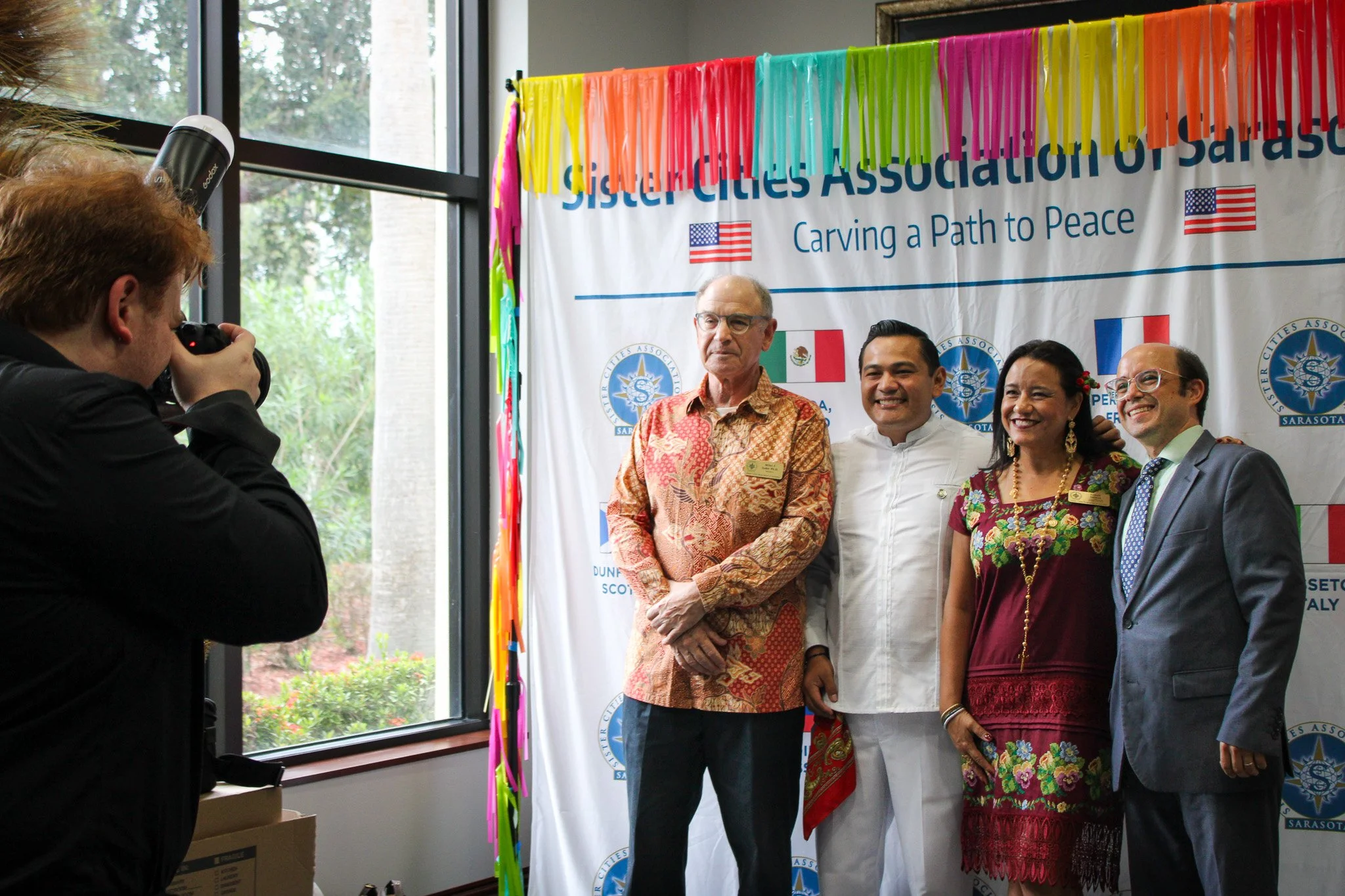 Open laptop displaying a collage of lifestyle photos, placed on a wooden desk with a potted plant, a copper mug, a closed book, some fairy lights, and a small notepad.