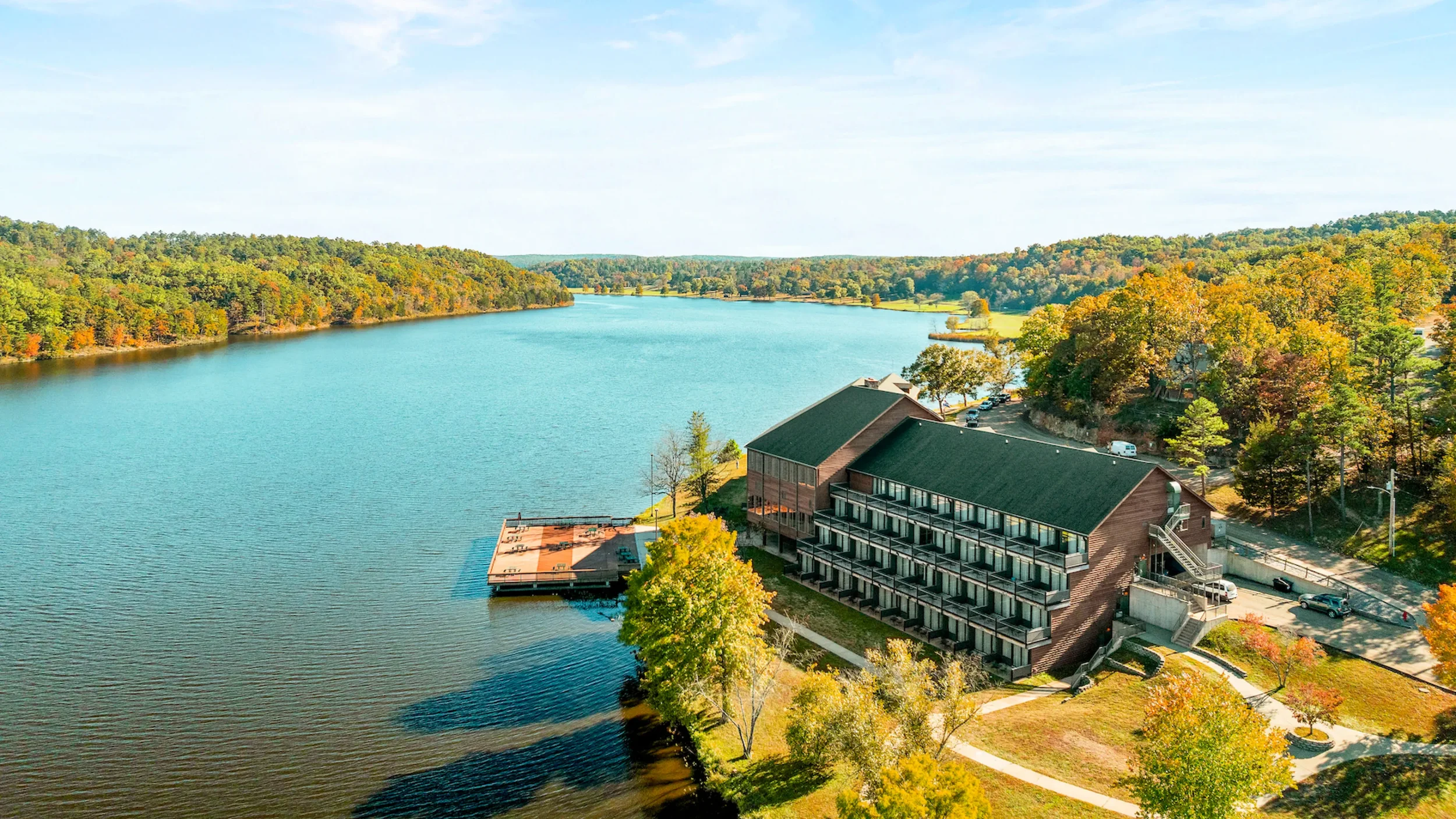 A large building surrounded by colorful fall trees near a lake.