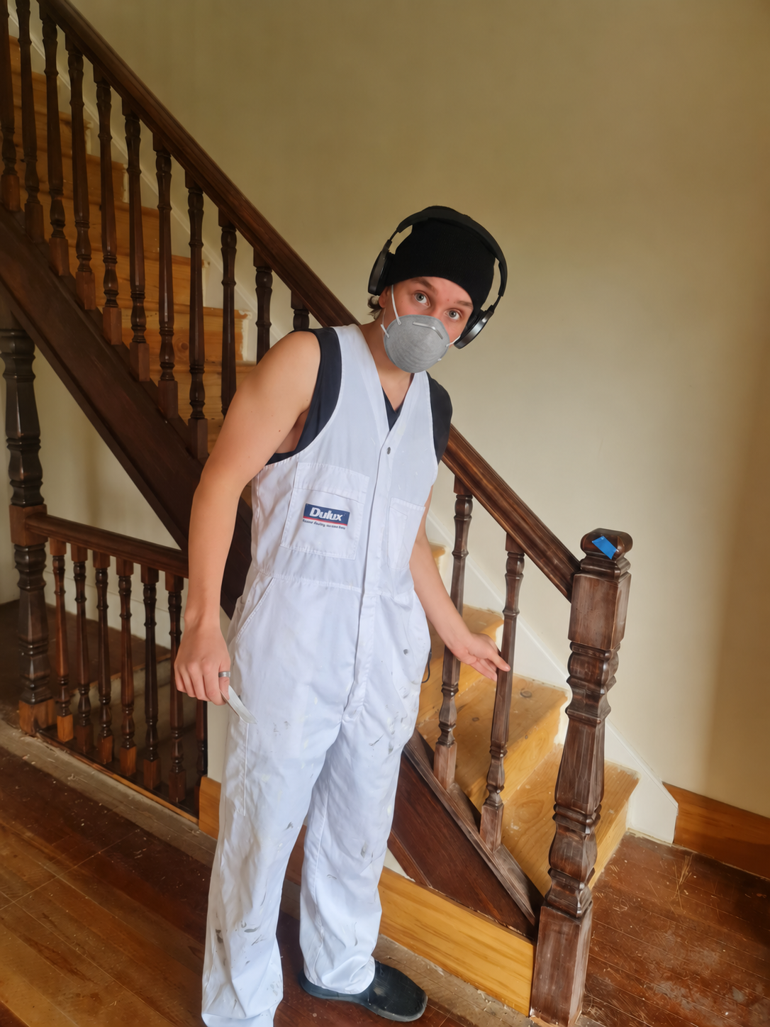 Painter wearing a dust mask and work overalls beside a timber staircase