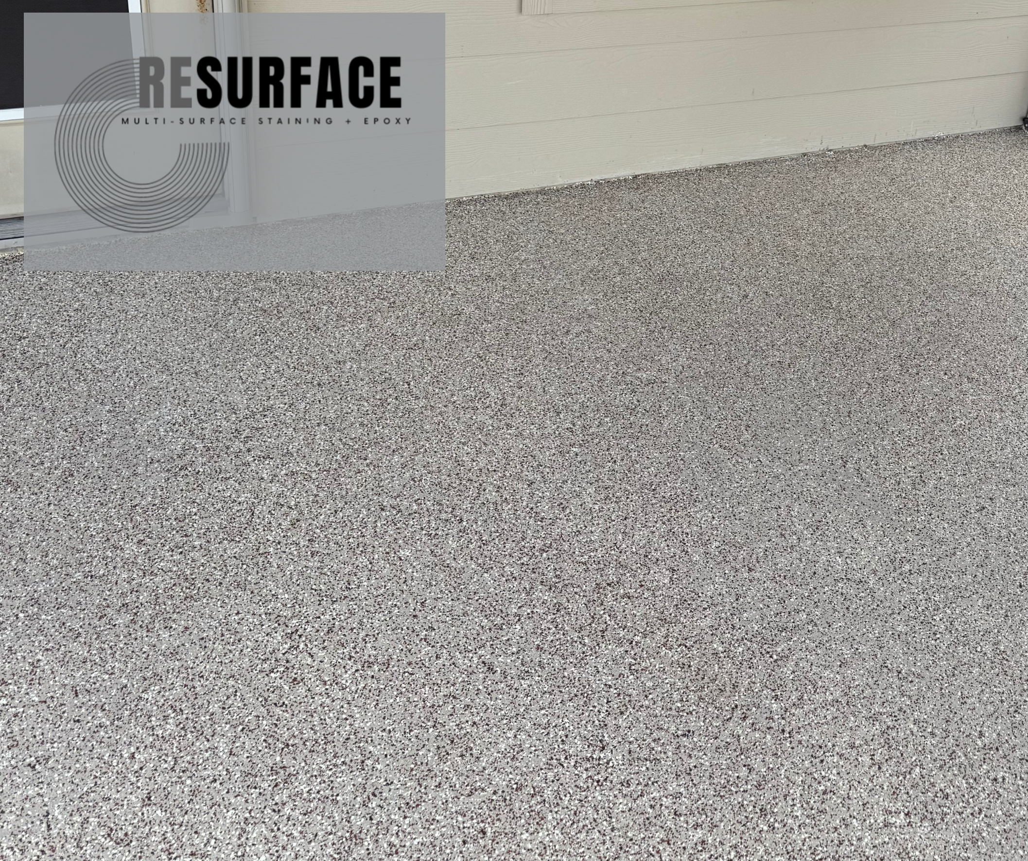 Close-up of a textured, multicolored epoxy-coated concrete floor in front of a beige wall and a white garage door