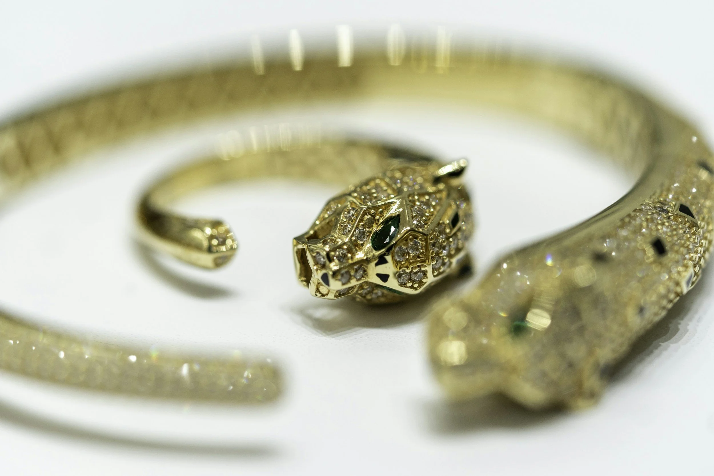 Close-up of a gold jewelry set featuring a ring and a bracelet, both decorated with numerous small diamonds and green gemstones, designed in a panther or animal motif.