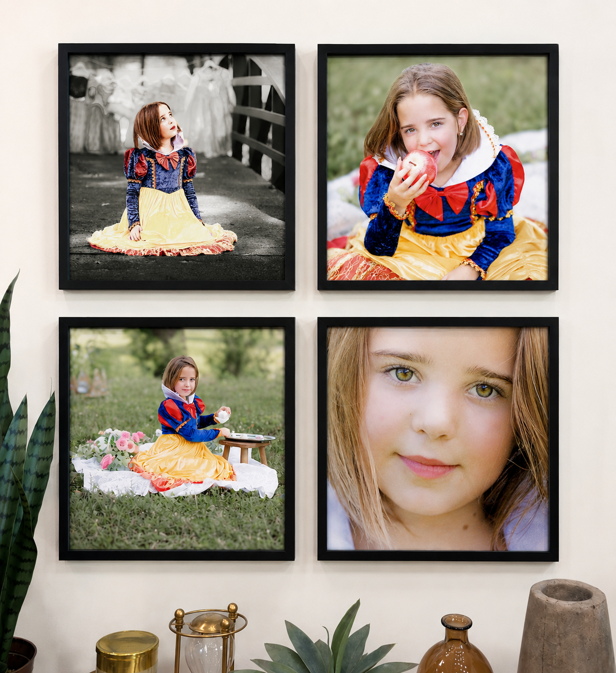 A gallery wall with four framed photos of a young girl in Snow White costume. The top left photo is in black and white, showing her sitting on a bridge looking up. The top right photo shows her smiling and eating an apple outdoors. The bottom left photo features her sitting on a blanket in a park, surrounded by pink flowers, holding a teacup. The bottom right is a close-up of her face with green eyes and light brown hair.