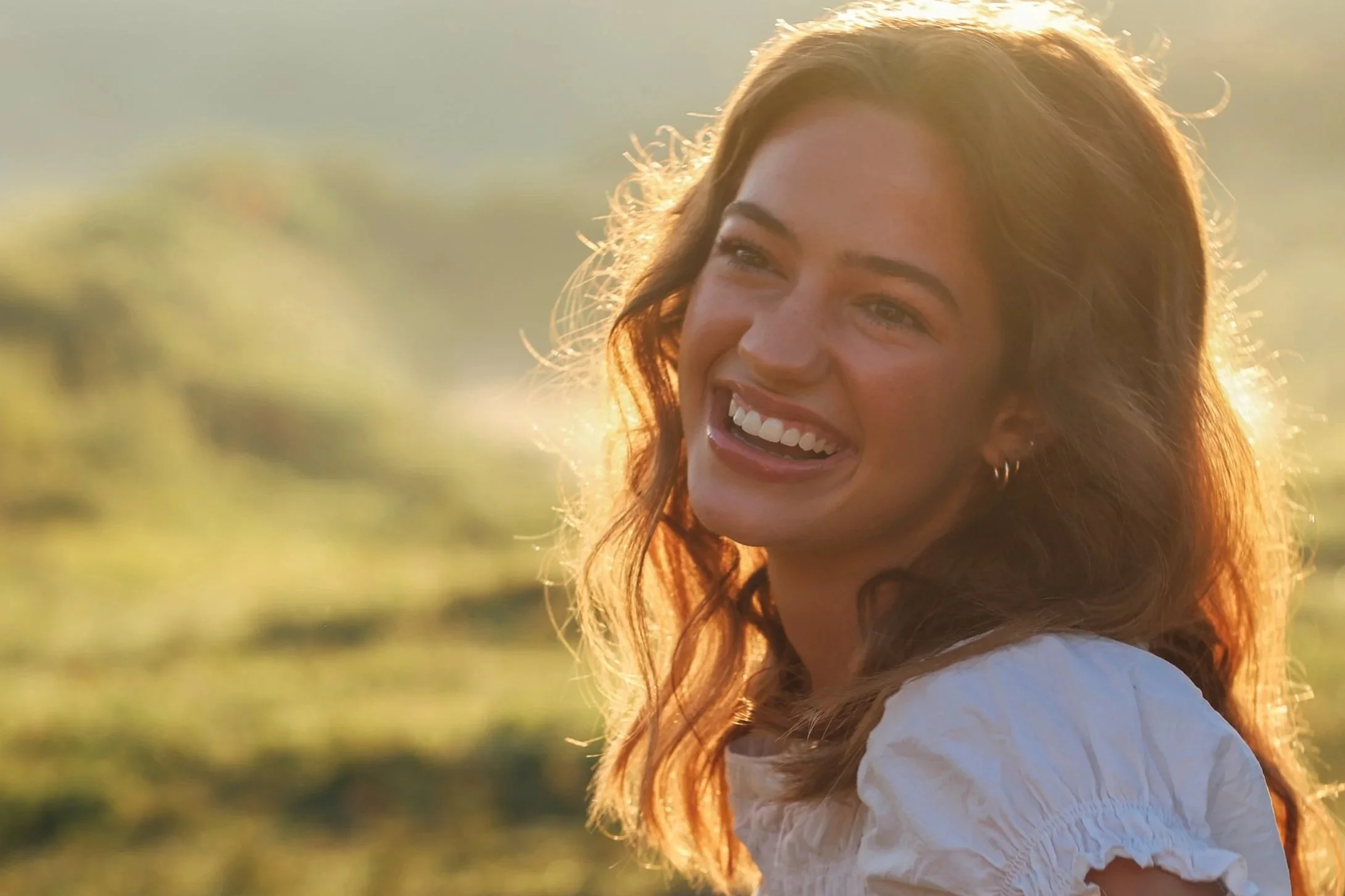 A woman with red hair smiling outdoors during golden hour