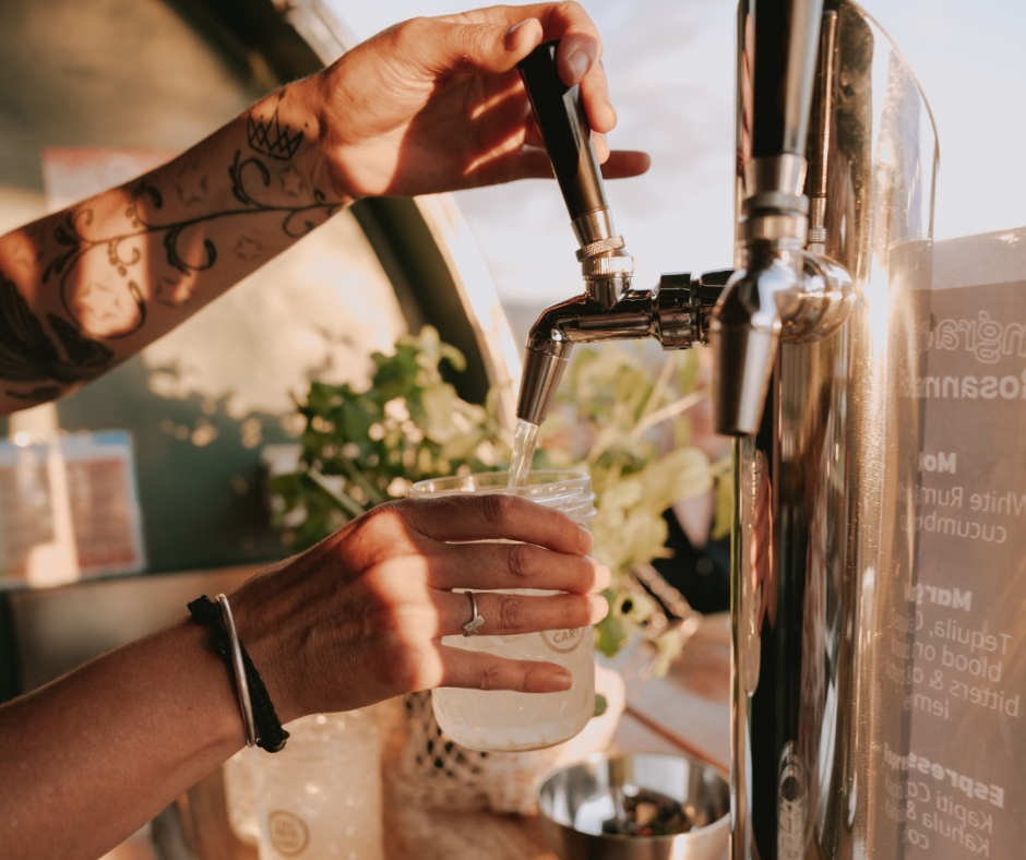 hand holding a glass with the other hand pulling the tap on a keg tap to pour a cocktail