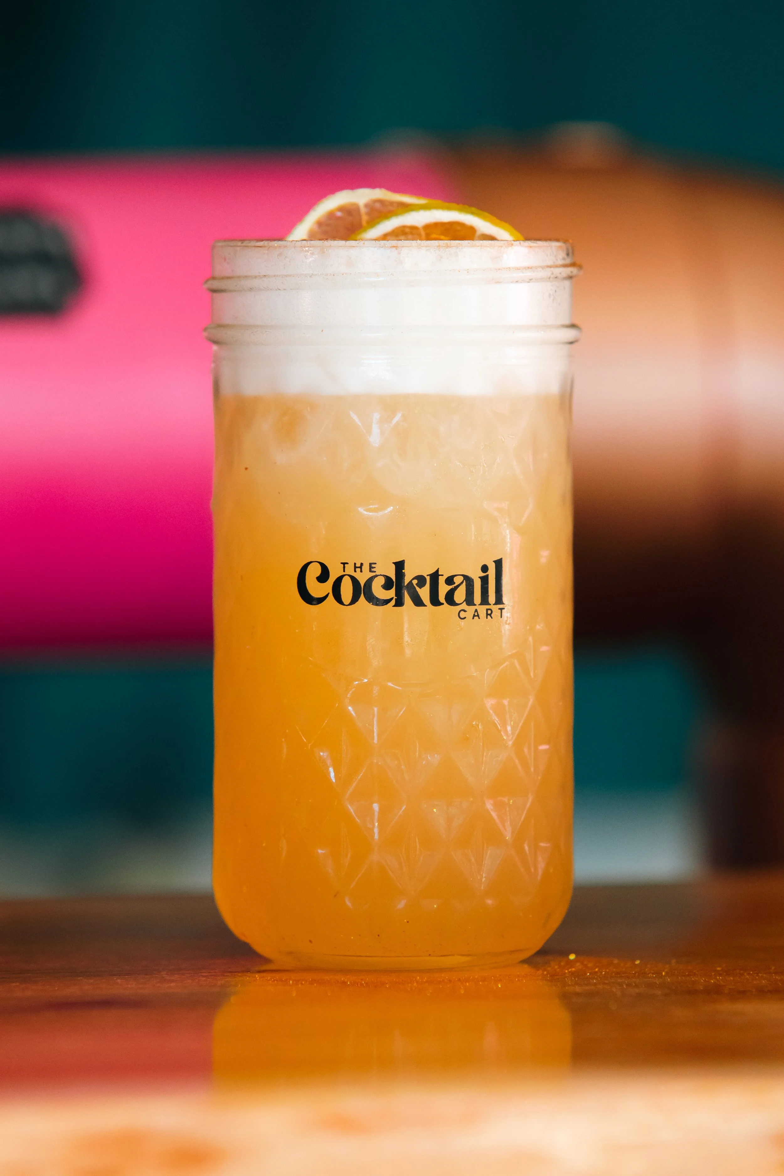 A mason jar with a yellow-orange beverage, garnished with lemon and orange slices, on a wooden surface.