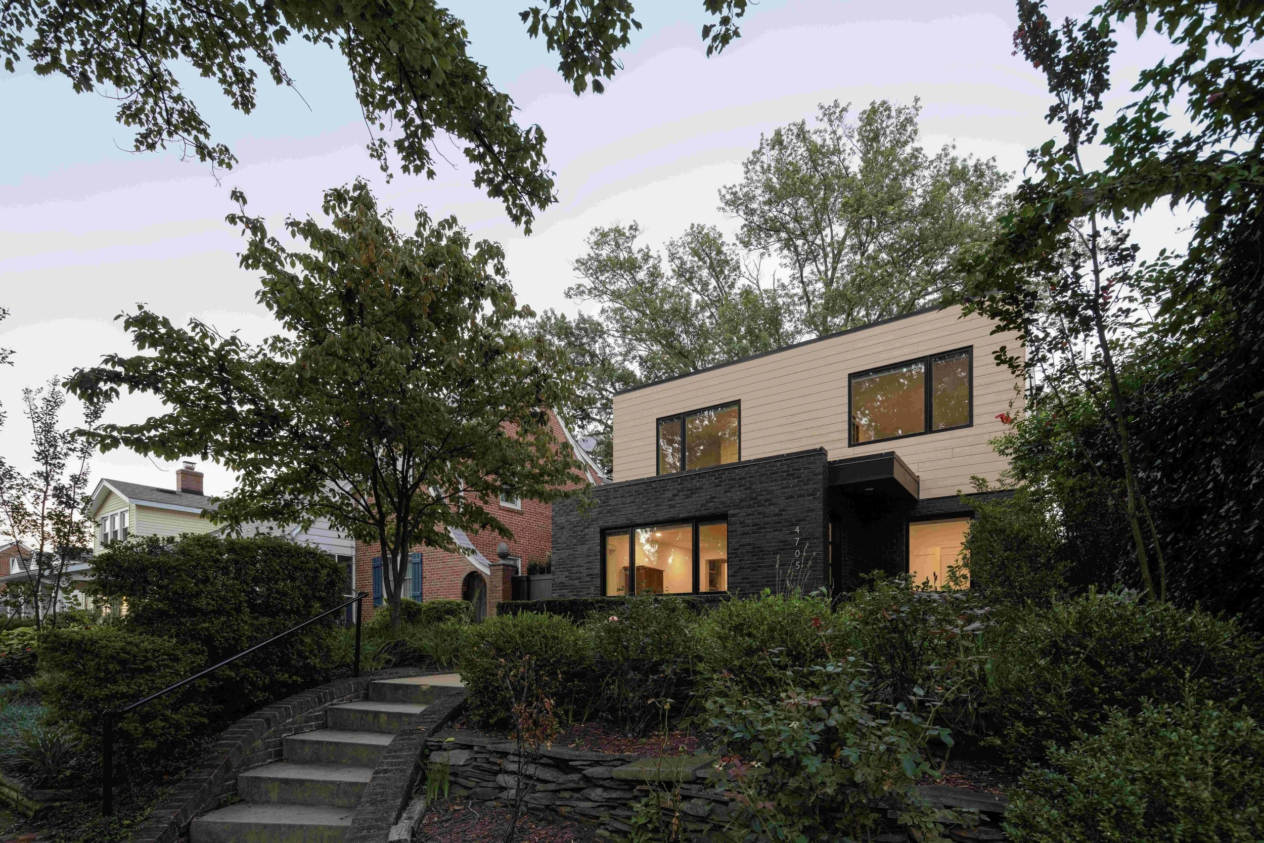 Two story house, black brick, beige siding, black windows, trees, dusk, modern design, flat roof