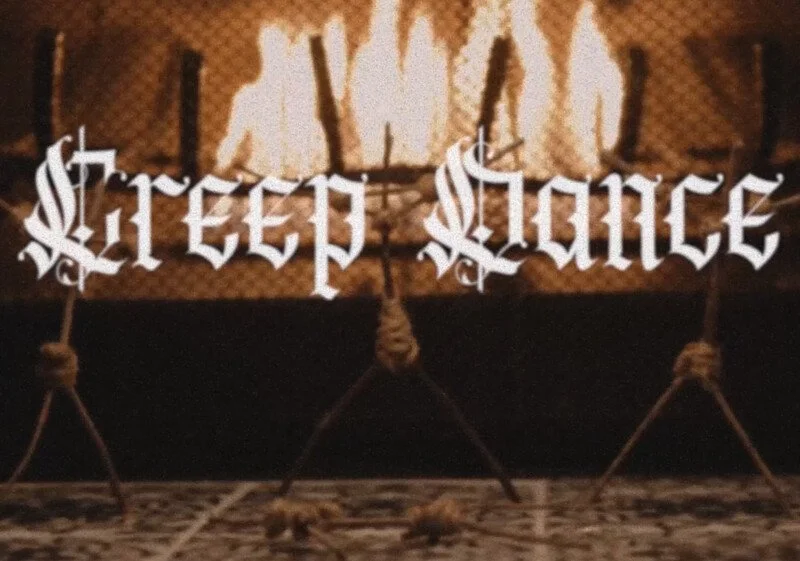 A firepit with flames behind a sign that reads 'Street Dance' in gothic font, supported by ropes and stakes.