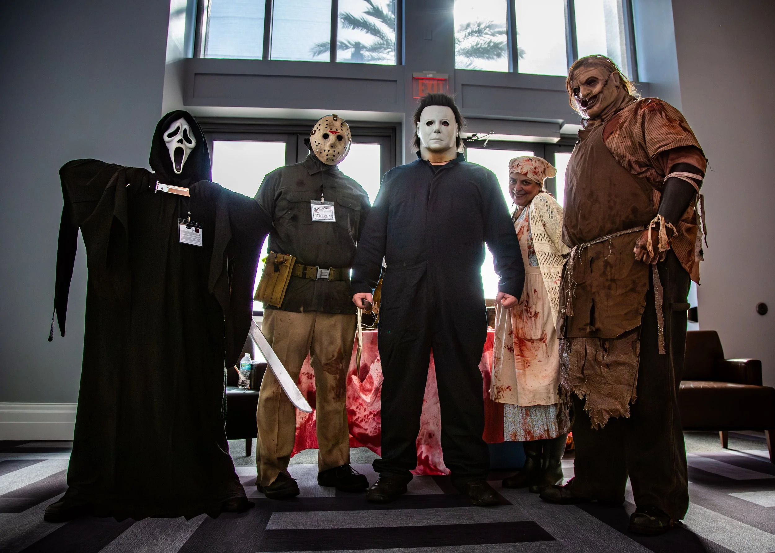 Group of people dressed in horror movie character costumes standing indoors near a window.