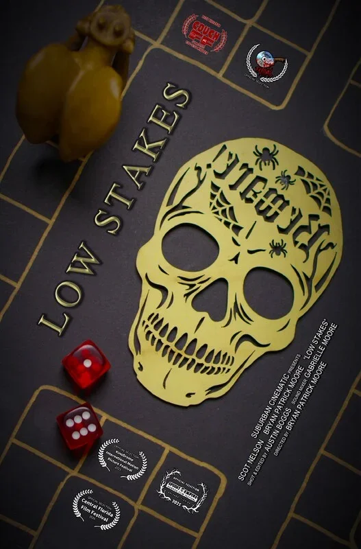 A Halloween-themed board game named "Low Stakes" featuring a yellow skull design, two red dice showing four and three, a spider web, and a orange monkey figurine on a dark surface.