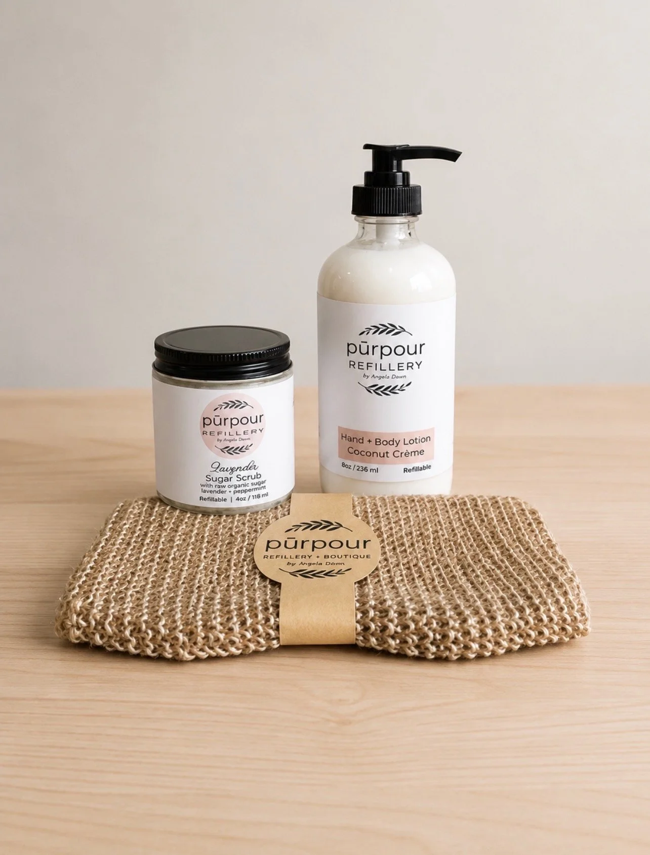 a bottle of refillable body lotion, a refillable jar of sugar scrub and a biodegradable bath mitt
