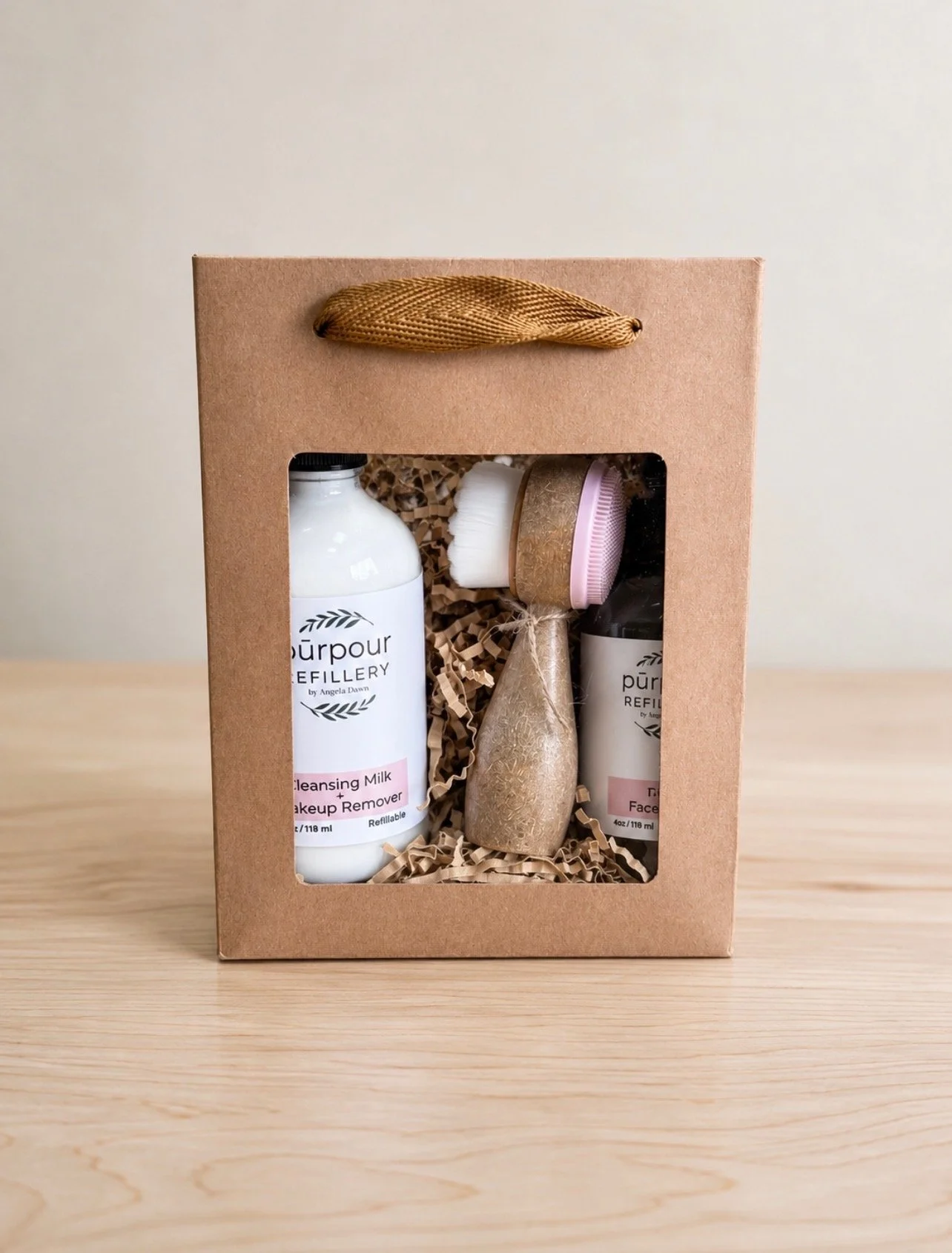a paper gift with a clear window revealing a bottle of cleansing milk/makeup remover, a bottle of rose facial mist and a facial cleansing brush