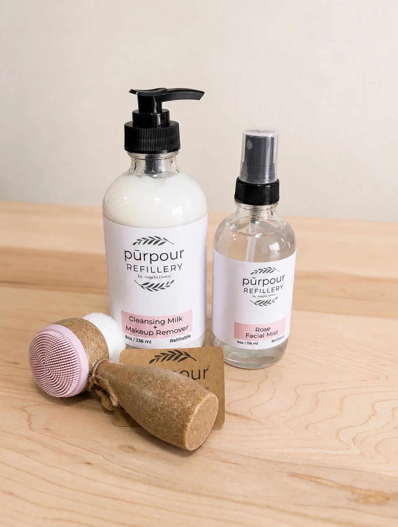 a bottle of cleansig milk + makeup remover, a refillable bottle of rose facial mist, and a facial cleansing brush