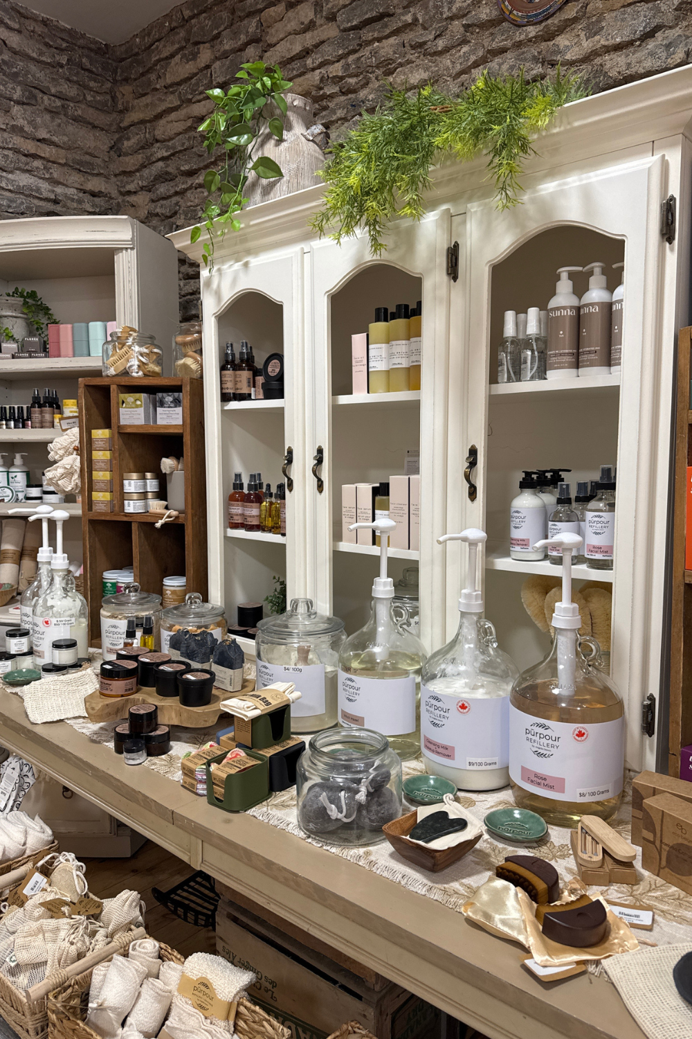 A long wooden table with large jugs of refillable products with personal care items in the foreground