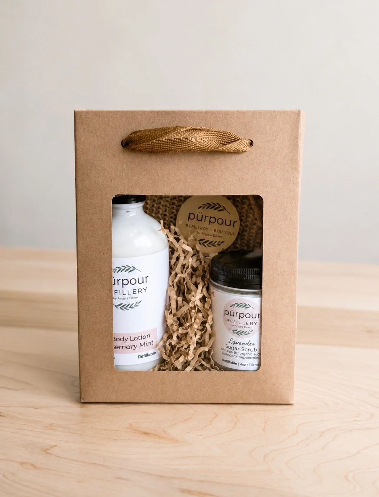a gift bag with a clear window revealing a bottle of hand and body lotion, a jar of sugar scrub and a biodegradable bathing mitt