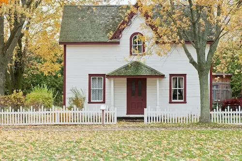 Cozy white house with a picket fence and autumn leaves, representing a peaceful respite care environment.
