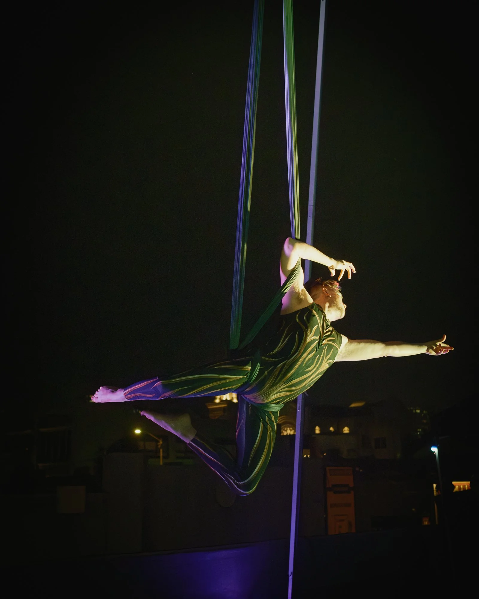 An aerial hammock performer in a striped outfit hanging from aerial sling during night performance in San Francisco