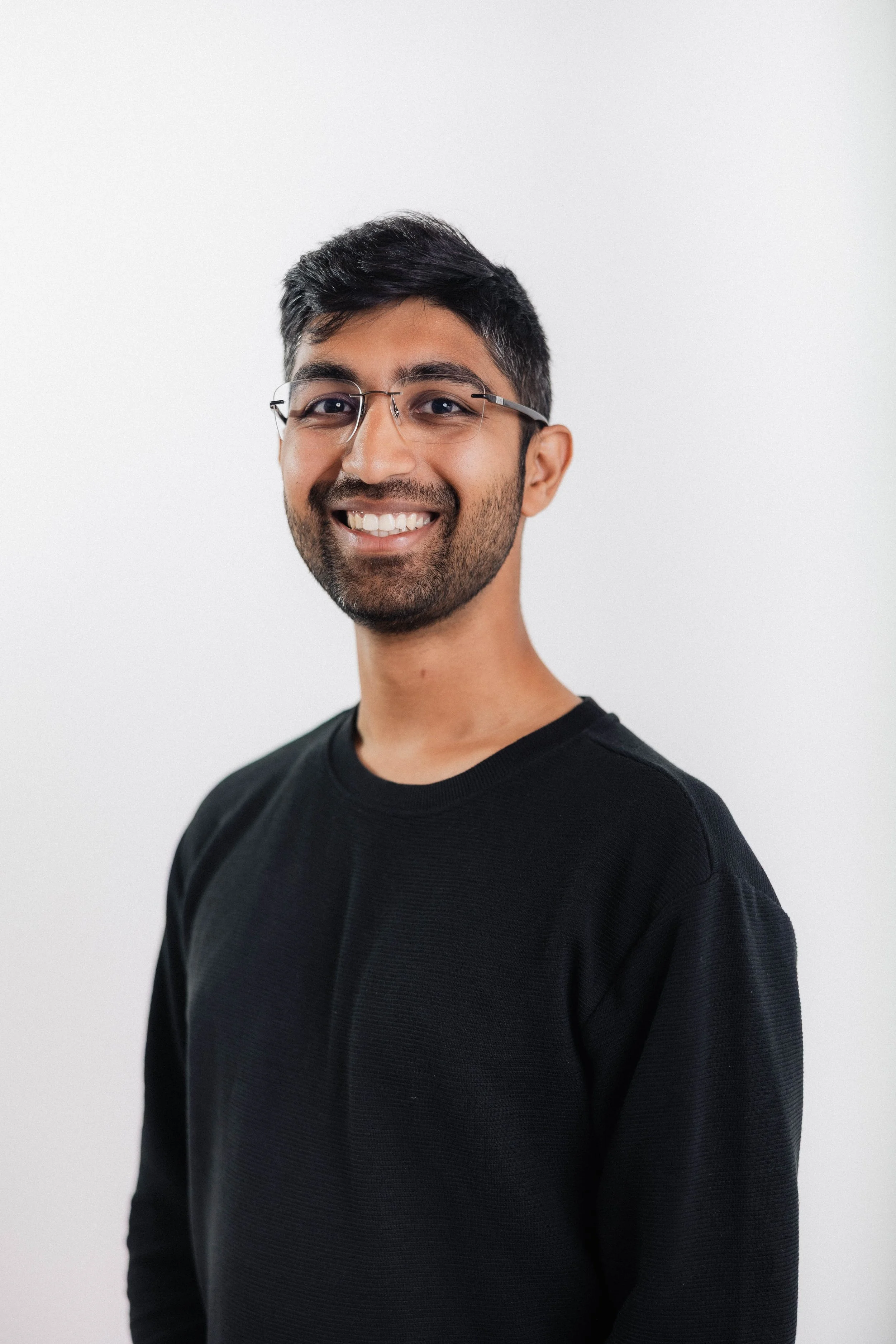 Portrait of a smiling man with glasses wearing a black shirt, standing against a plain white background.