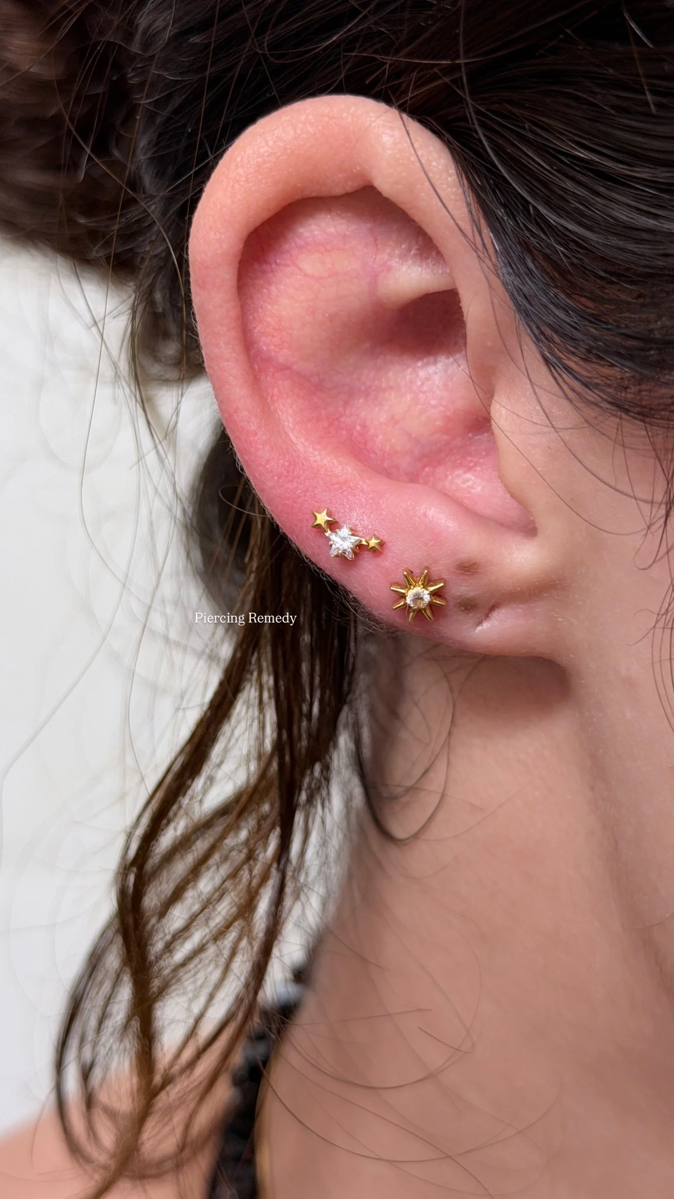 Close-up of a woman's ear showing three gold and diamond earrings with star and sunburst designs.