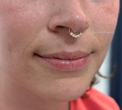 Close-up of a woman's face showing a nose piercing with a curved jewelry piece decorated with small stones.