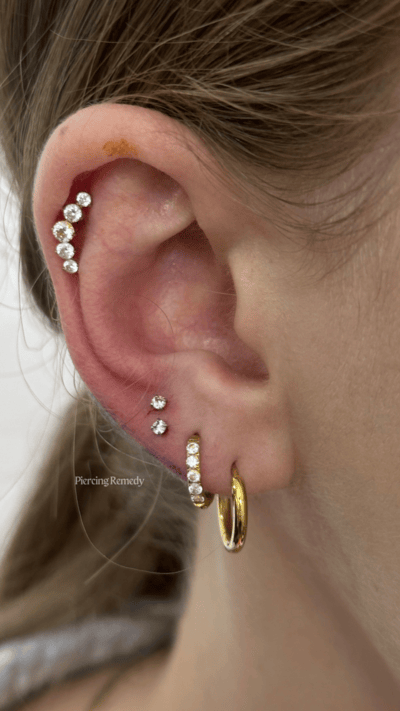 Close-up of a person's ear with multiple earrings, including a gold hoop and several small diamond stud earrings.