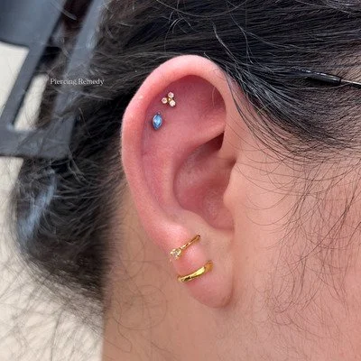 Close-up of a person's ear with multiple piercings, including three earrings and two small decorative gemstones.