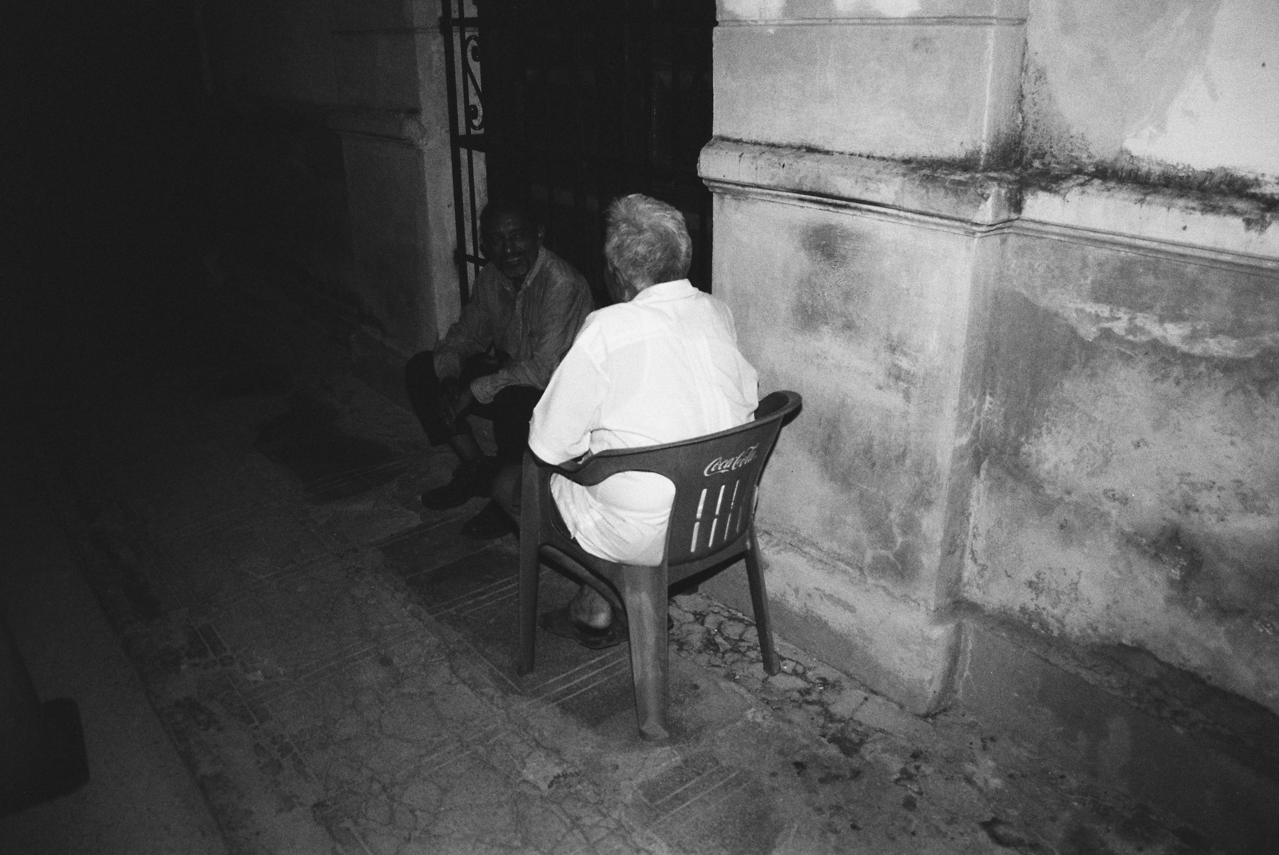 Black and white night photography of two men conversing on a sidewalk, existential street scene. 35 mm black and white film.