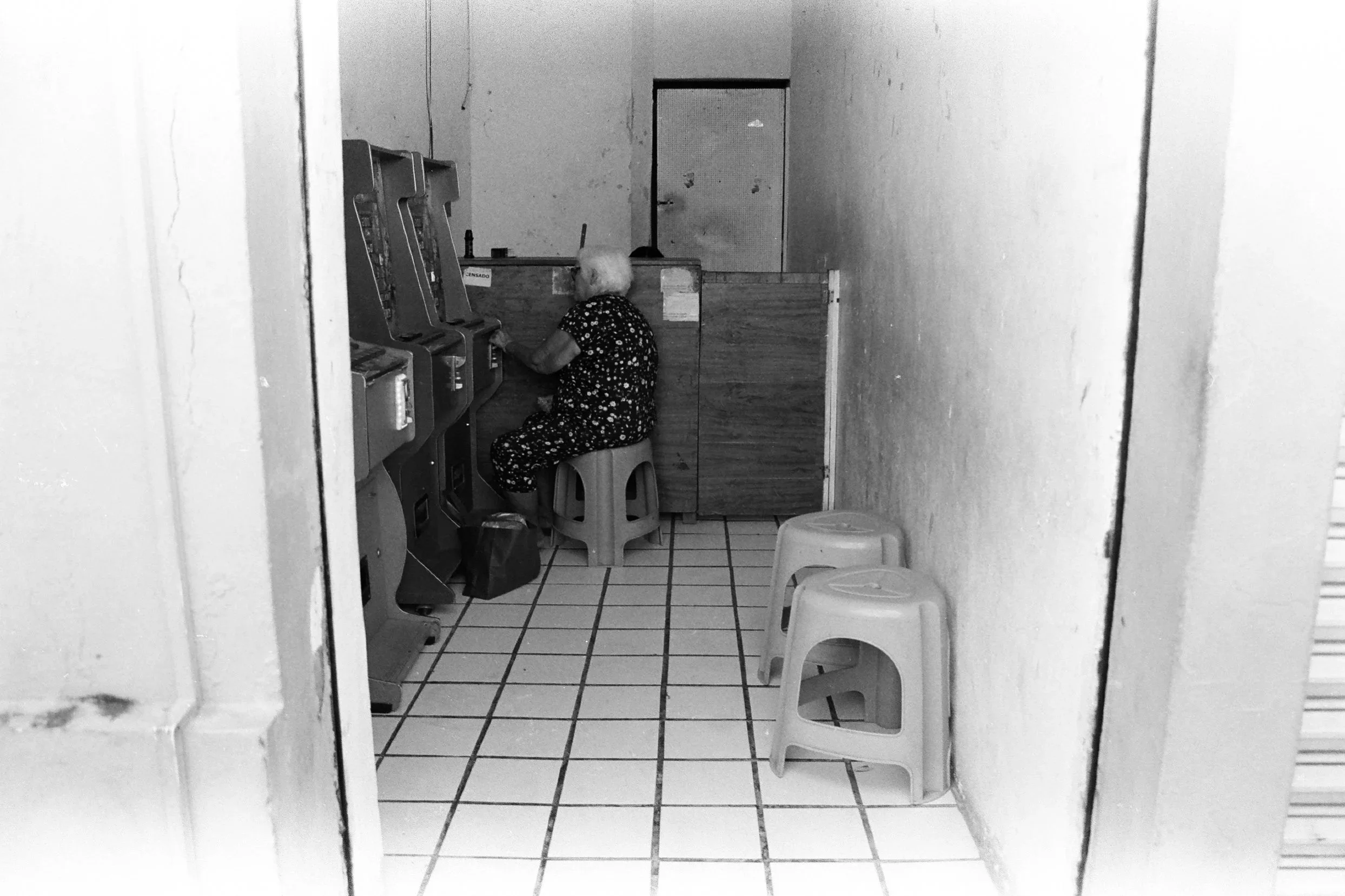 Black and white shot of an elderly woman playing arcade games alone in a dark interior. 35 mm black and white film.