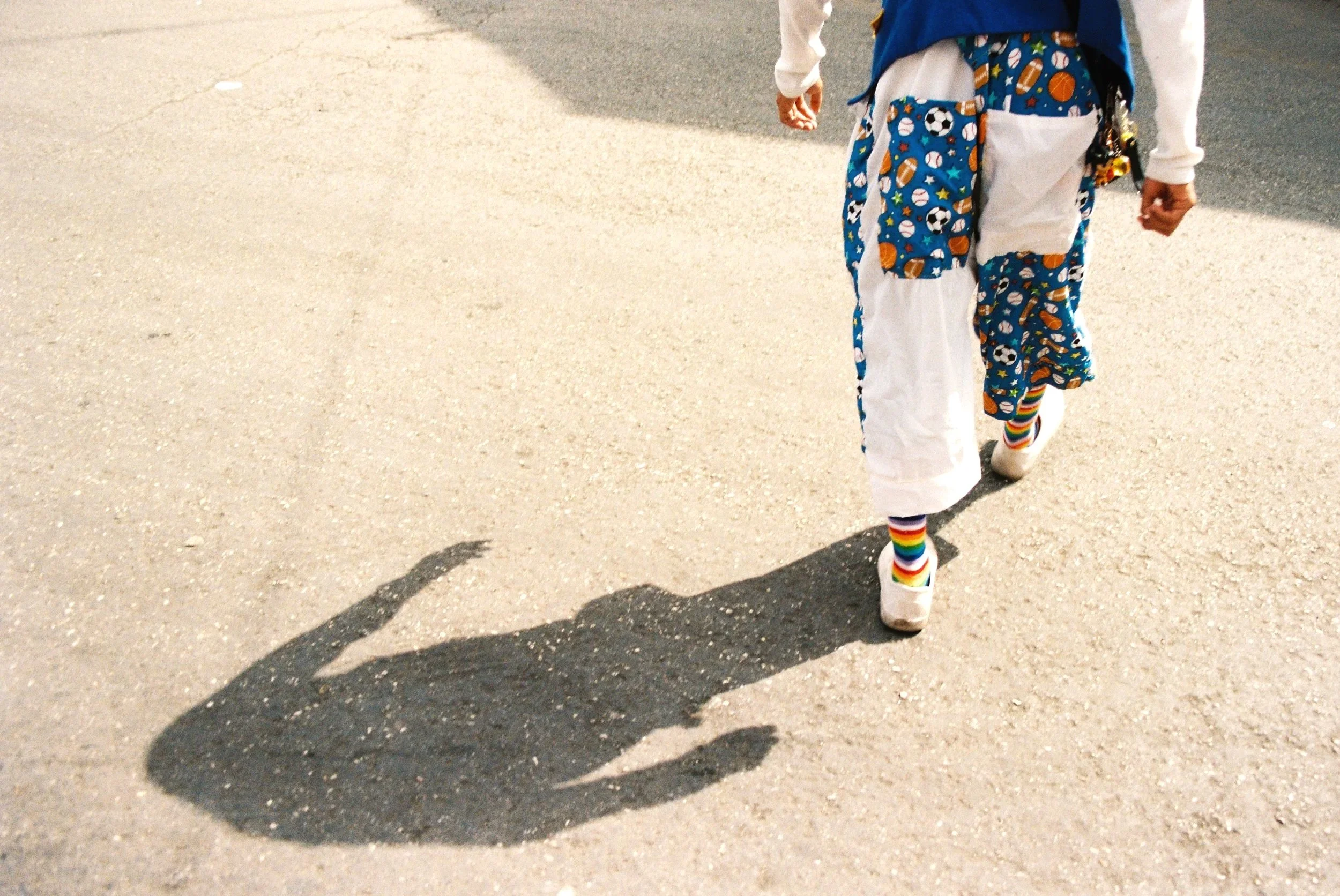 Top-down view of a person walking on asphalt wearing bright, colorful patterned socks. 35 mm color film.