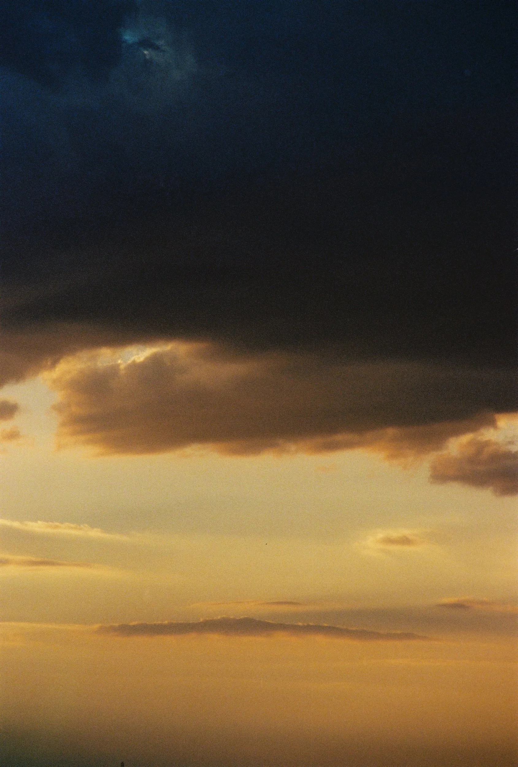 Wide shot of heavy dark clouds over a pale yellow sunset, documenting the atmospheric weight of a breakup. 35 mm color film.