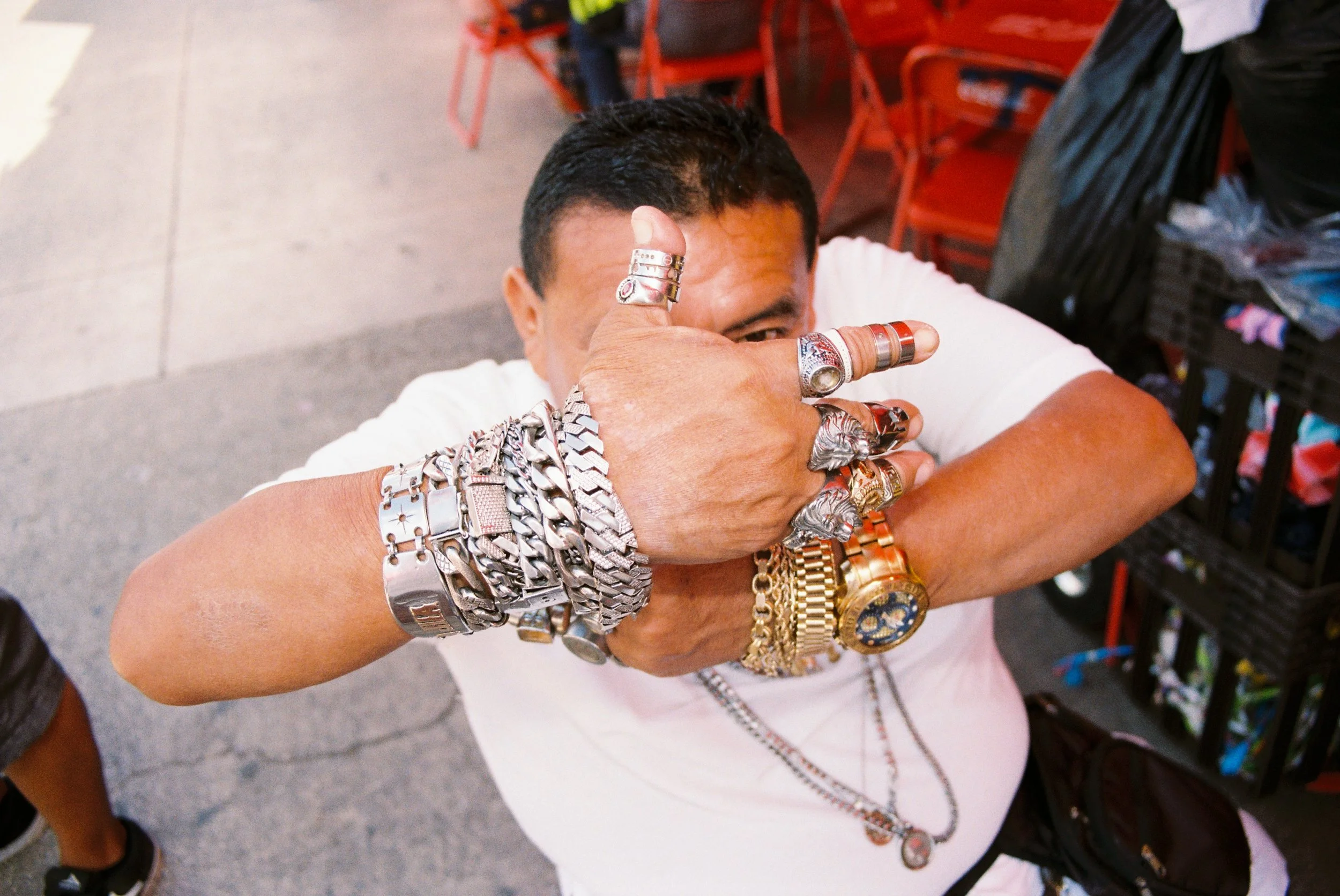 Portrait of a man covering his face with hands heavily adorned with gold and silver rings and bracelets. 35 mm color film.