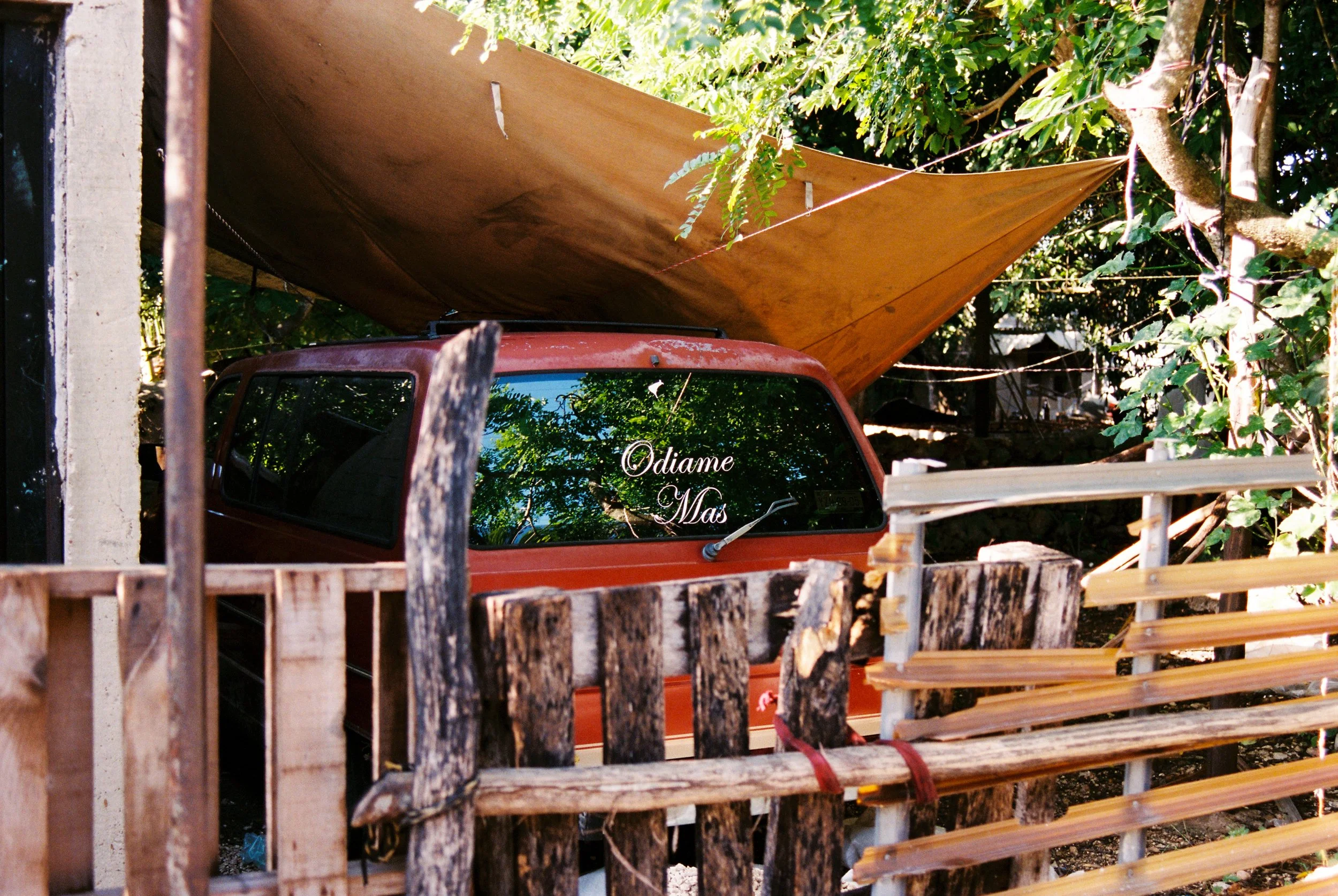 Close-up of a red van's tailgate featuring the phrase 'Odiame más' in white cursive typography. 35 mm color film.