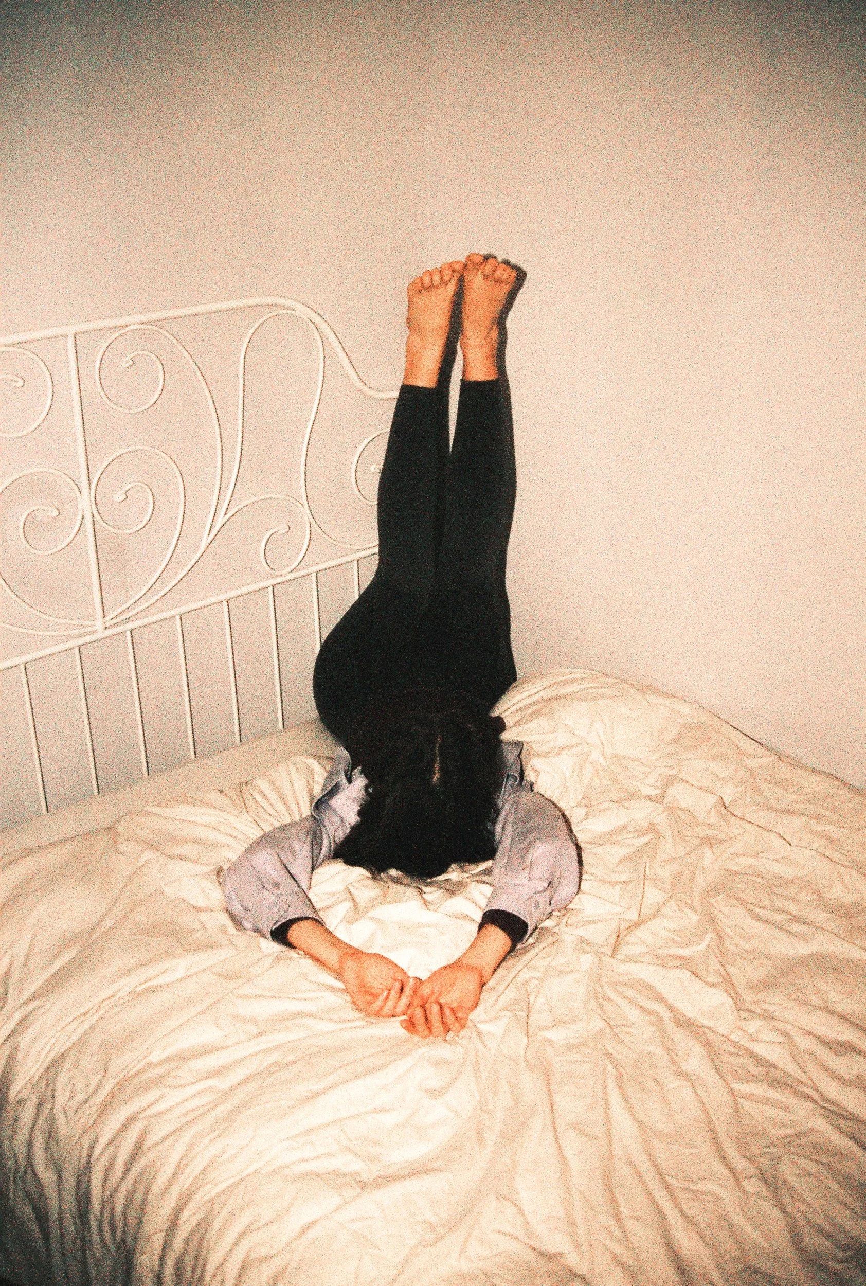 A person lying face-down on a bed with legs against the headboard, an intimate portrait of emotion. 35 mm color film.