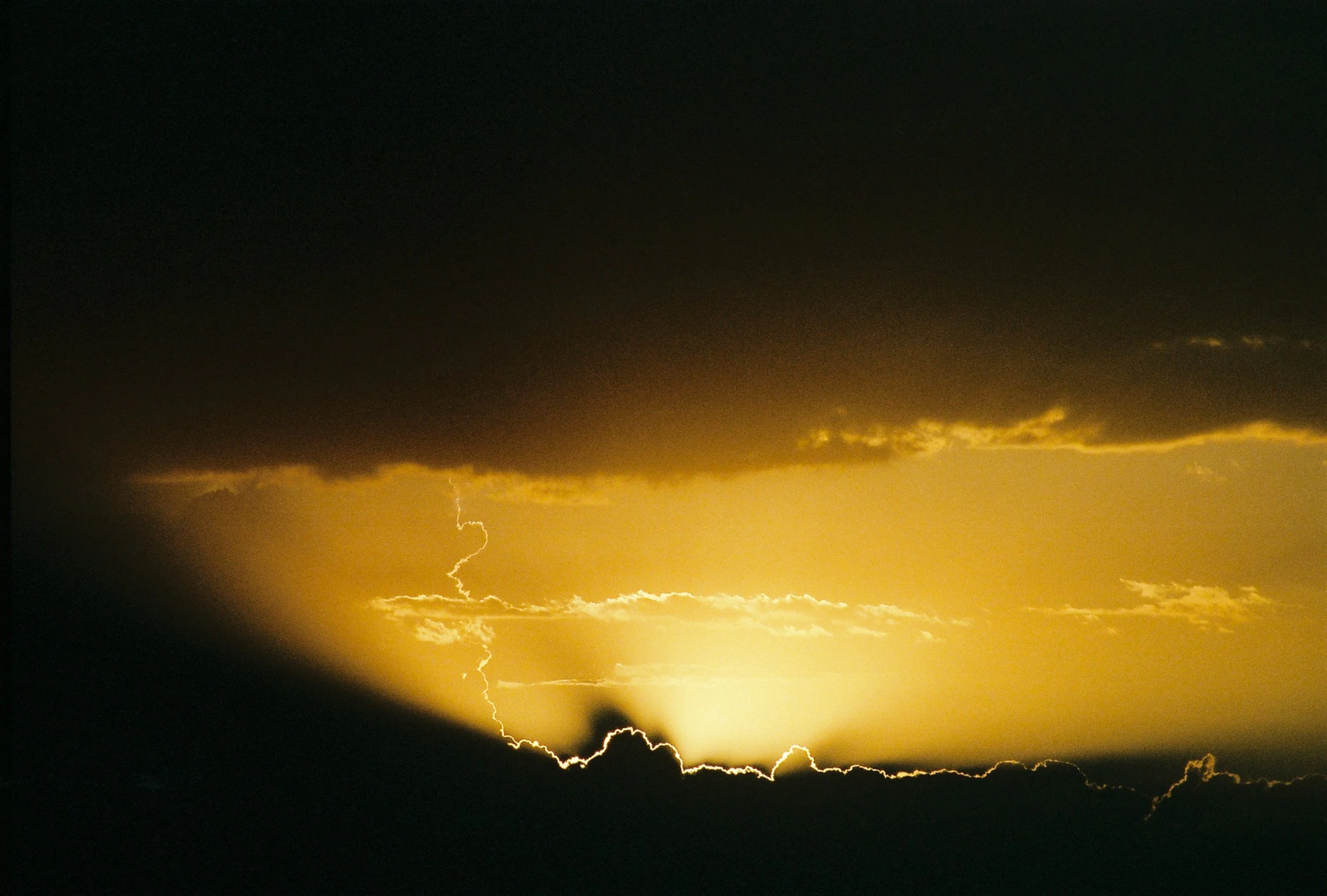 A violent lightning bolt striking through a heavy golden sunset, serving as an external reflection of internal heartbreak. 35 mm color film.