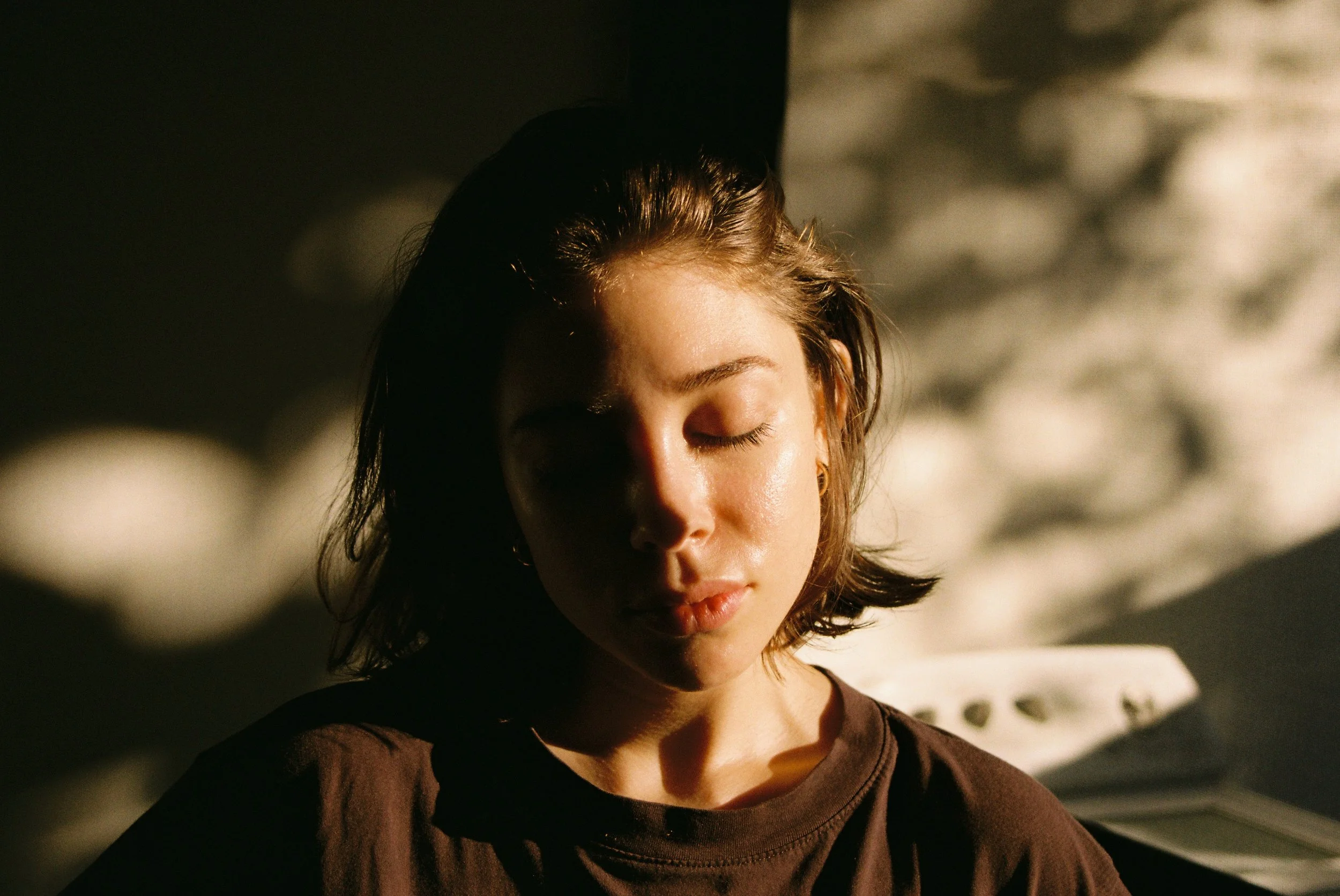 Warm, sun-drenched analog portrait of a her with closed eyes, evoking a moment of fleeting peace and intimacy. 35 mm color film.