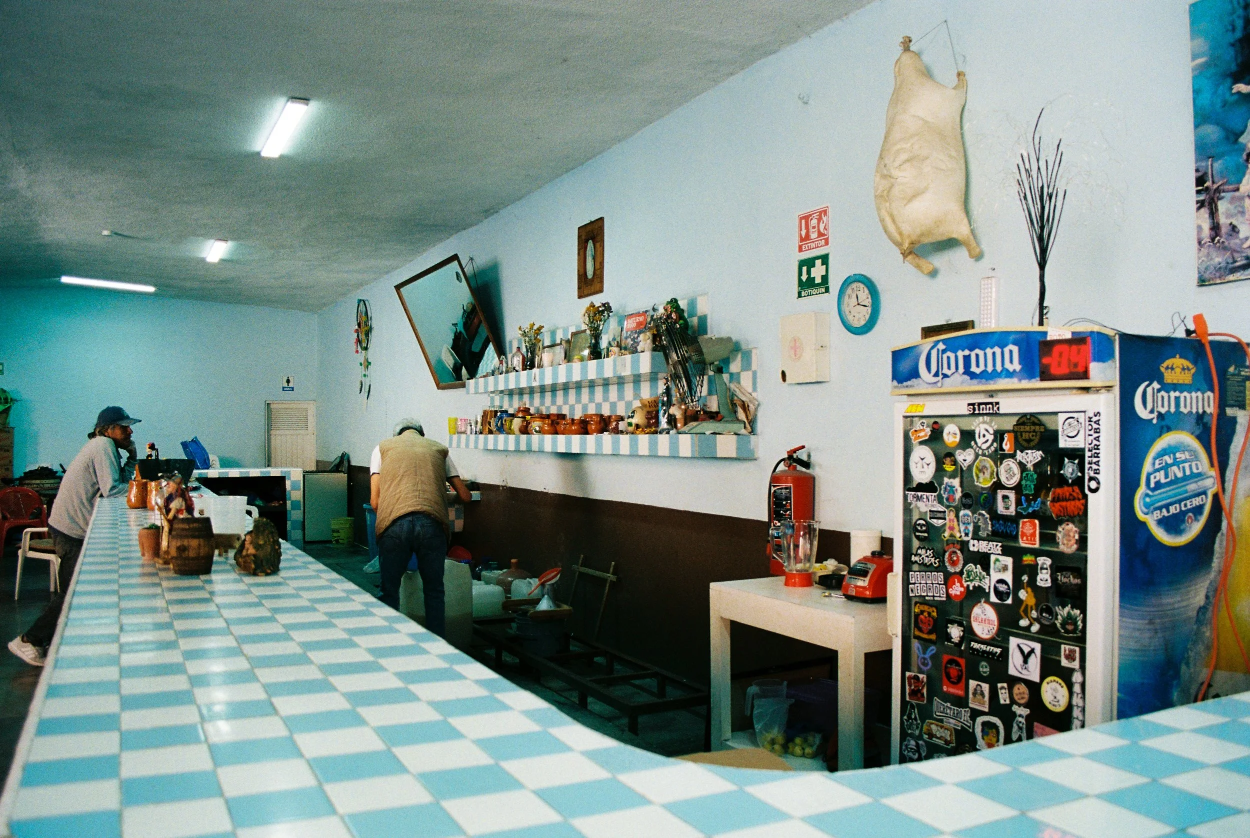 Interior of a Mexican cantina with blue tiled bar, a beer cooler, and a tilted mirror, cinematic style. 35 mm color film.