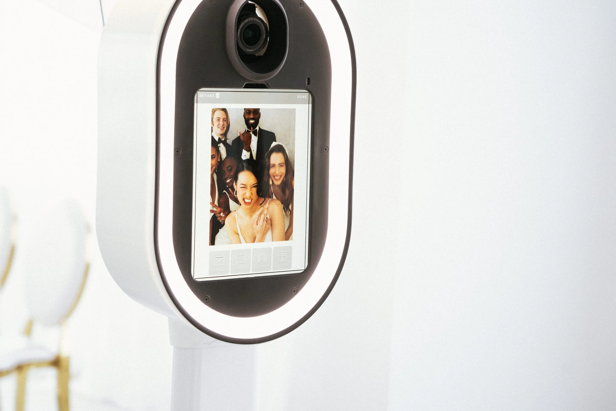 Photo booth camera displaying a photo of six people dressed in party attire, making funny faces and posing together.