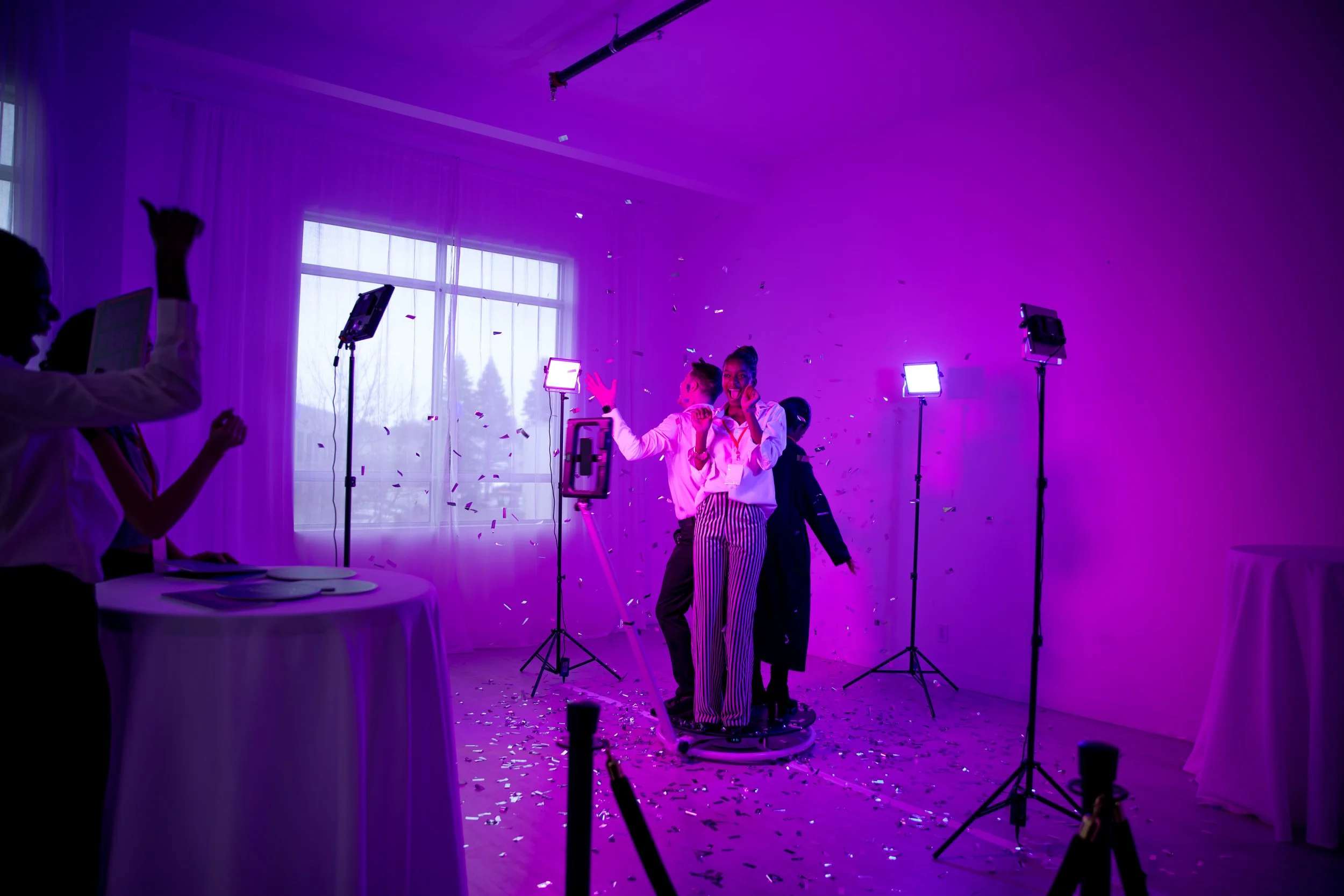 3 people standing on a 360 photo booth at a neon party throwing confetti 