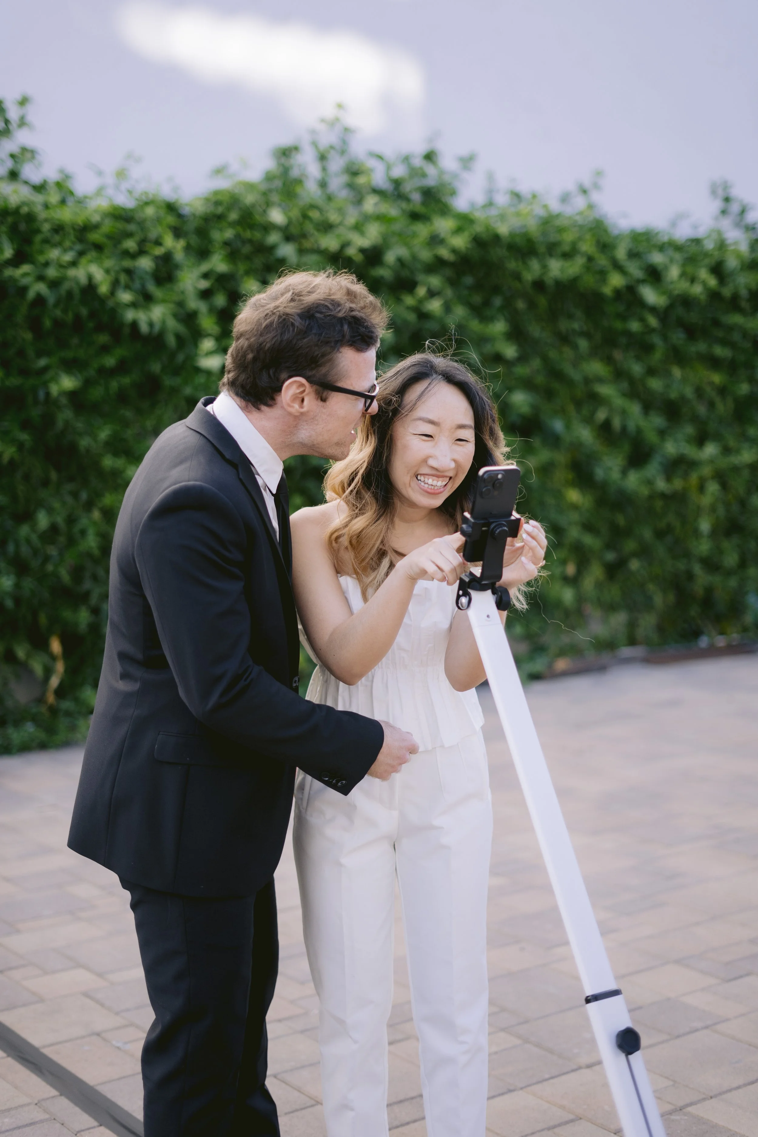 a couple at a event using a 360 photo booth outside with a green hedge behind