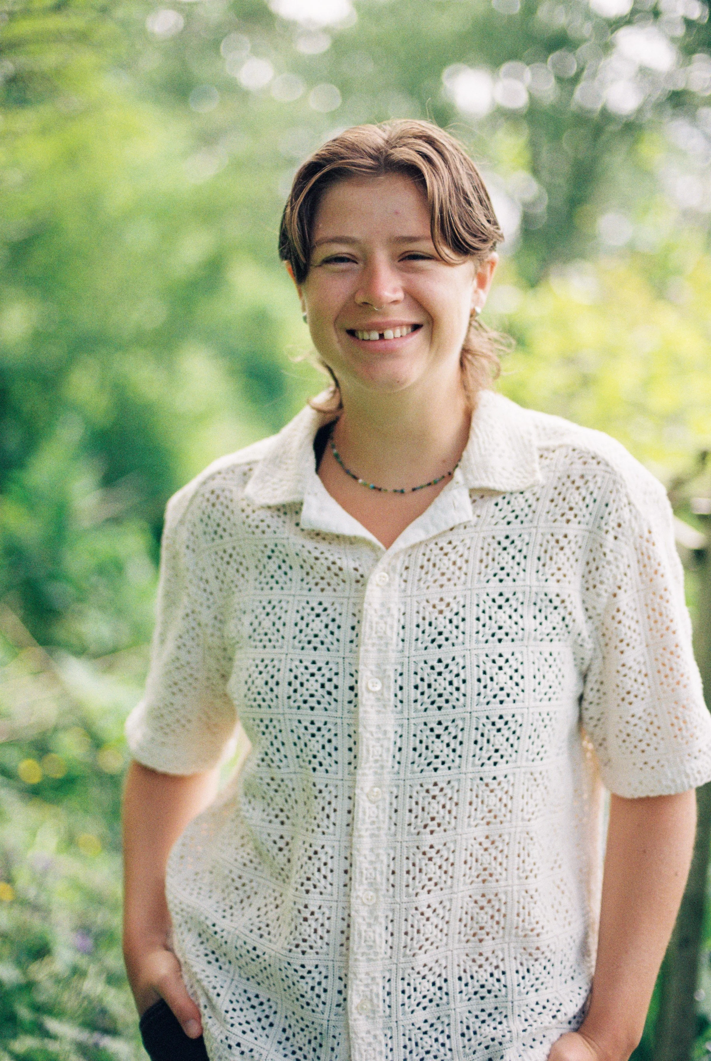 A woman with short brown hair smiling outdoors with a blurred green background.