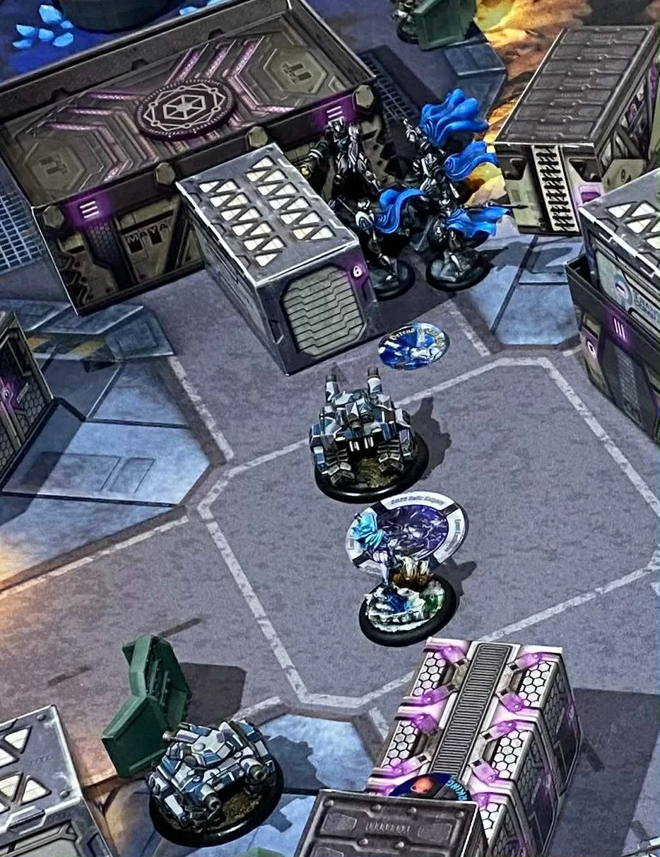 A tabletop game setup with miniature figures and terrain pieces, including buildings, vehicles, and bases, for a sci-fi or futuristic strategy game.
