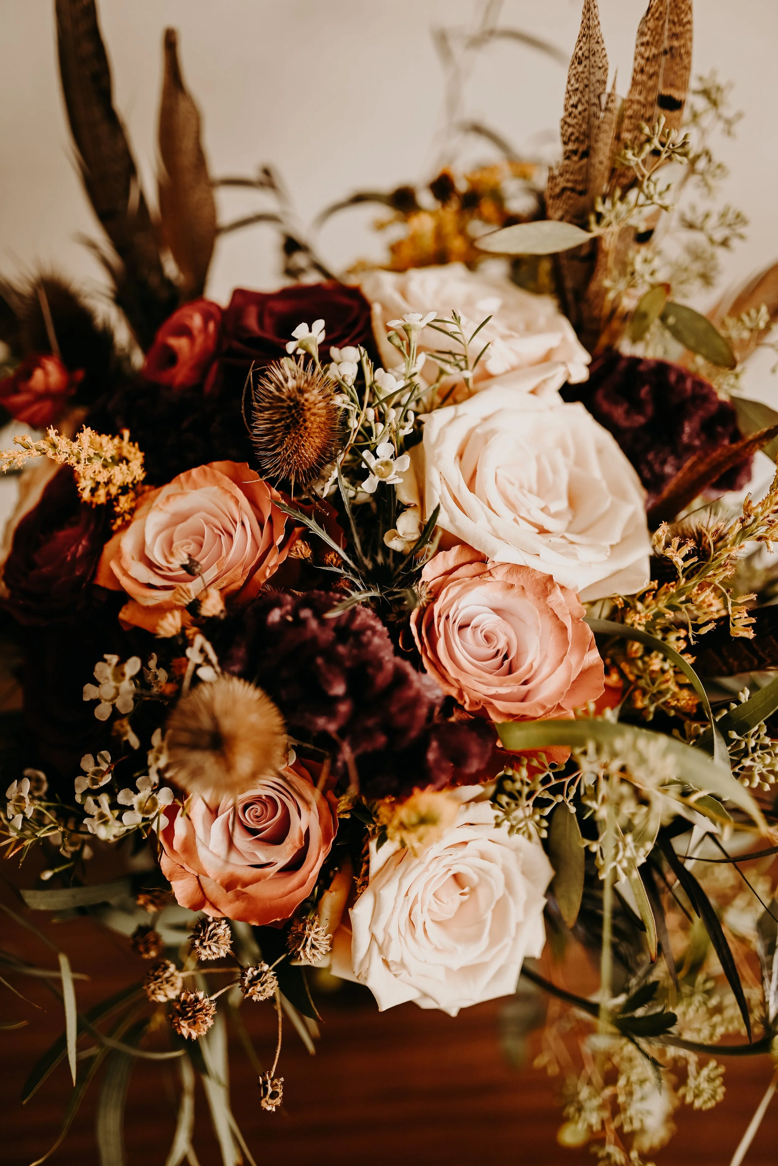 A bouquet of mixed roses, dried flowers, greenery, and natural elements arranged in an elegant floral display.