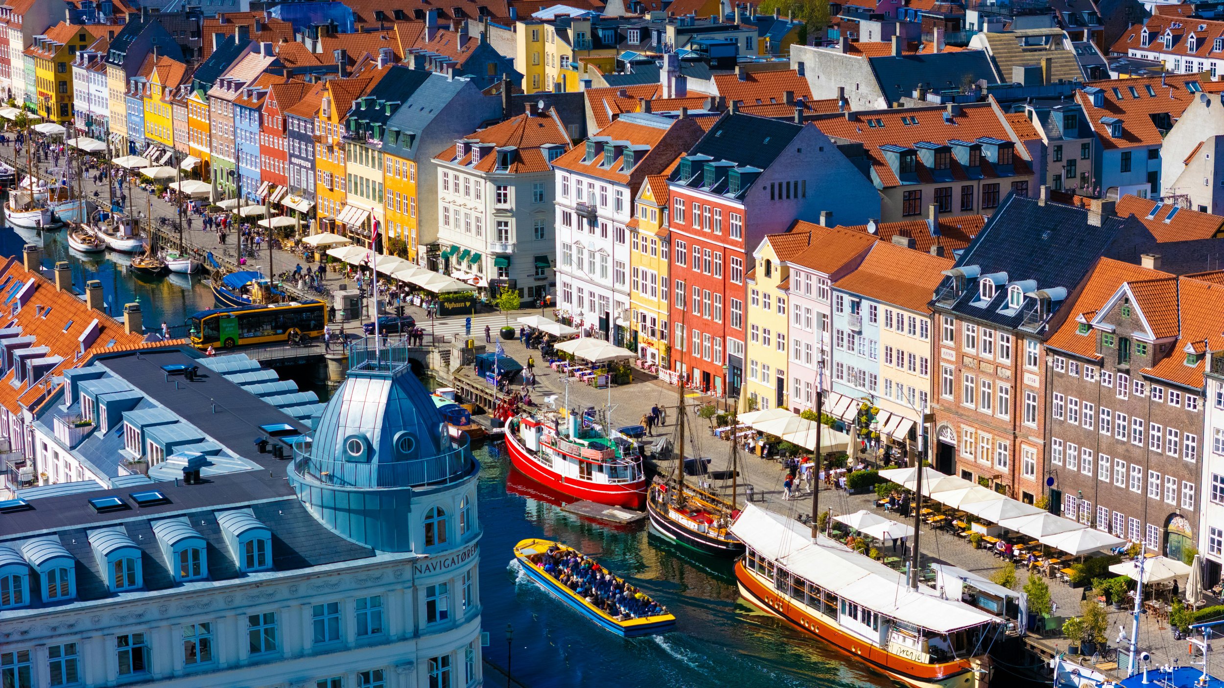 Colorful buildings lining a waterfront with boats and outdoor cafes, capturing a lively harbor scene in a European city.